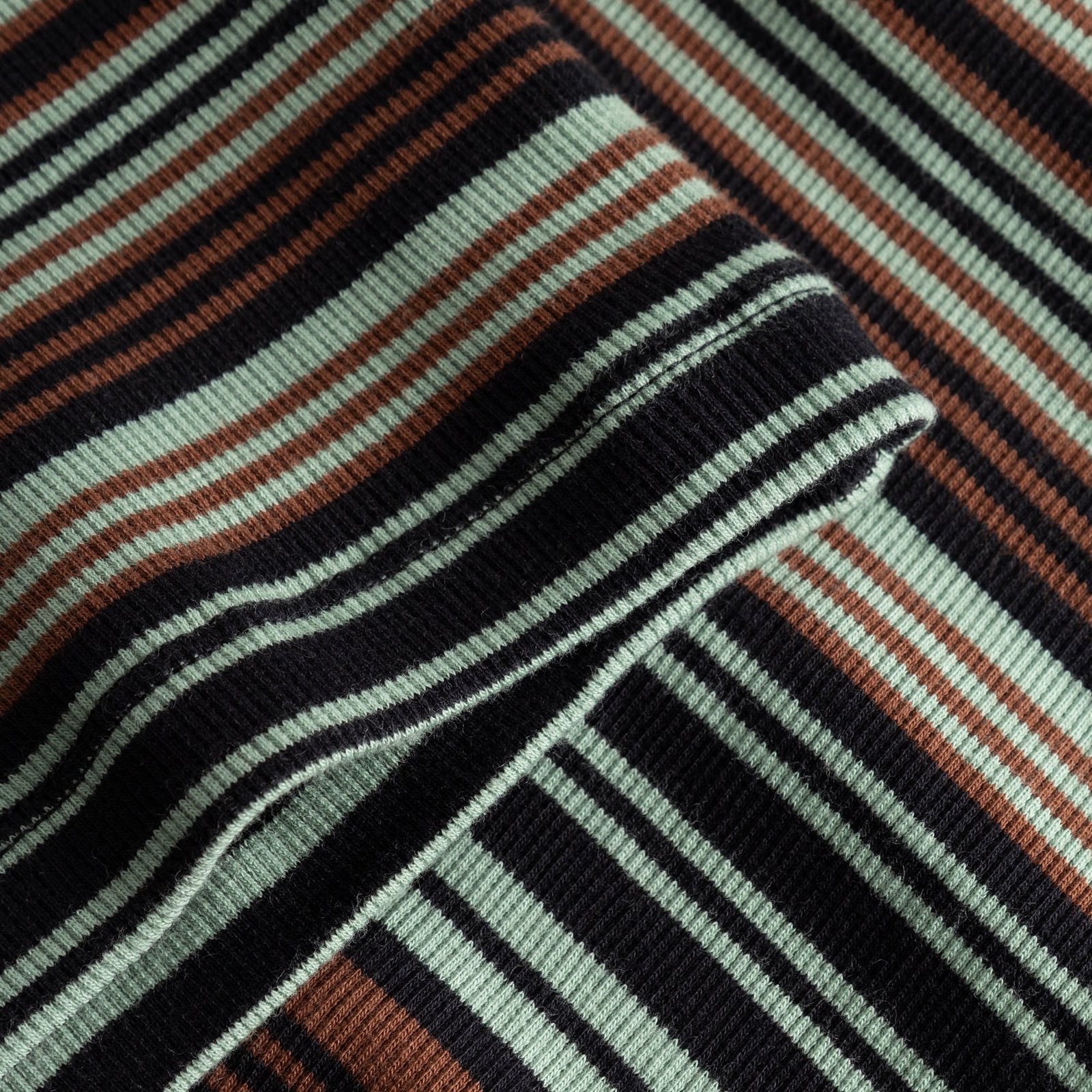 Close-up of the Rib Dress Lunsen showing the soft ribbed fabric with irregular stripes in green, black and brown.