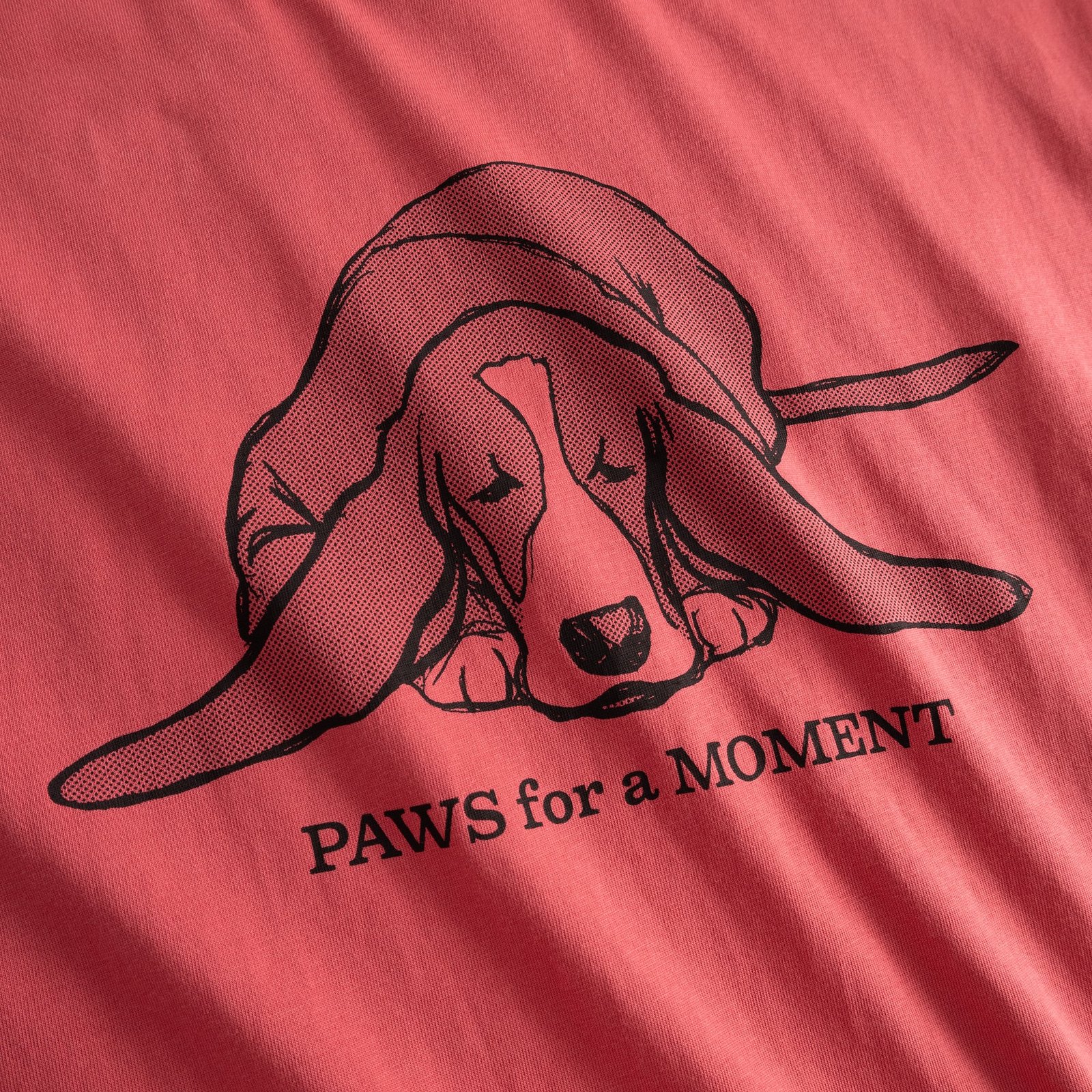 Close-up of the Paws for a Moment print on a holly red t-shirt, featuring a charmingly sleepy Basset Hound.