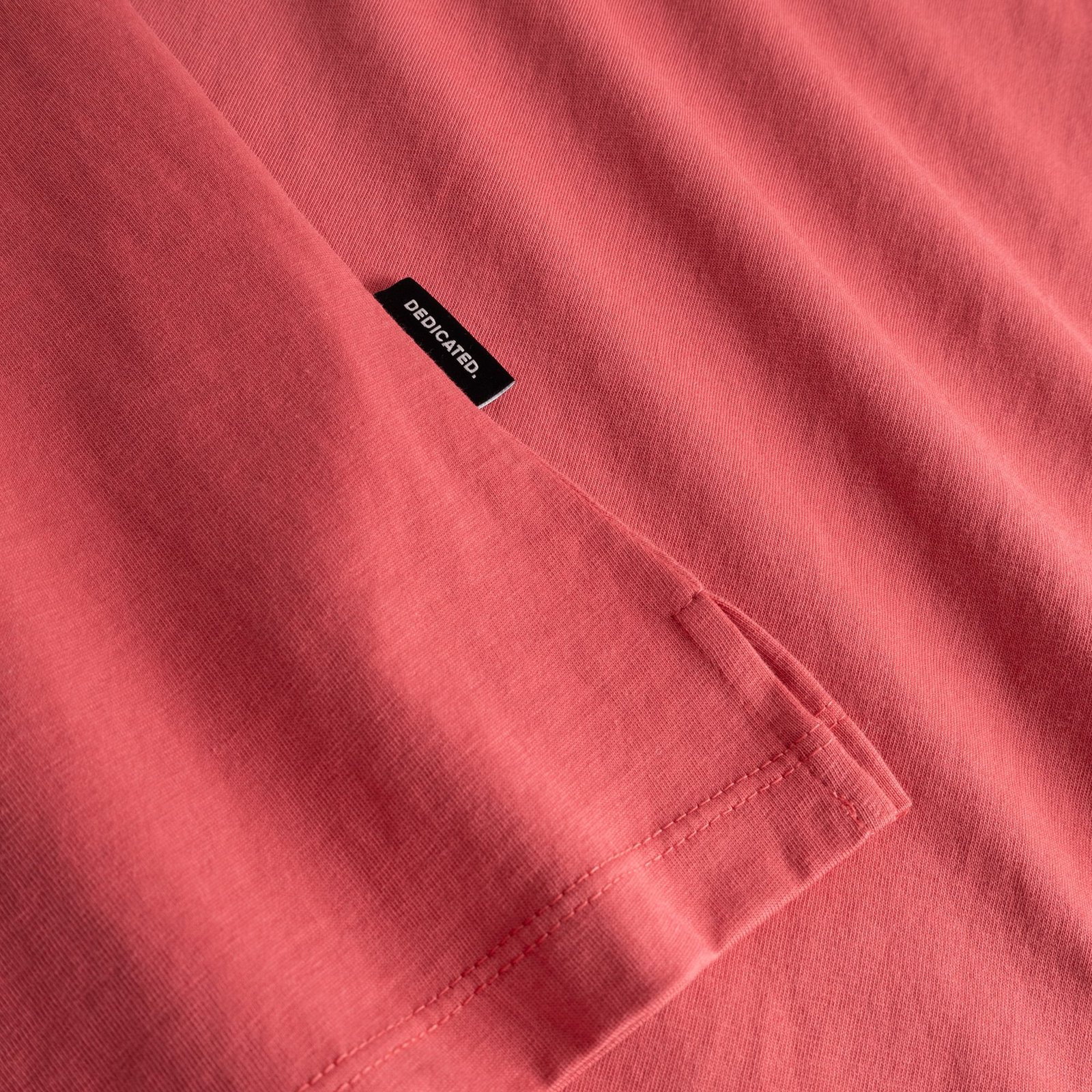 Close-up detail of the Visby T-shirt in Holly Red, showing the side slit and the subtle Dedicated brand tab.