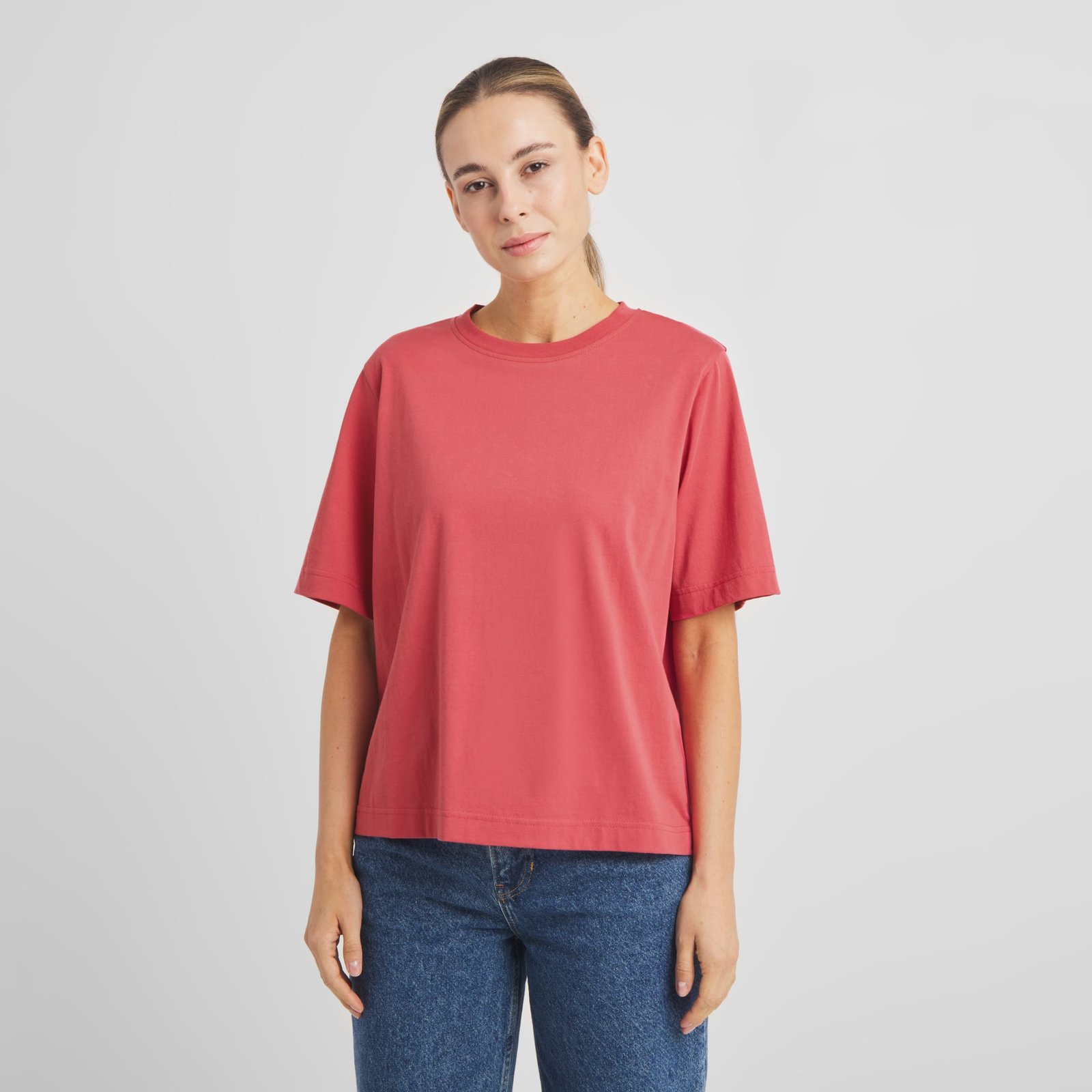 A woman models the relaxed-fit Vadstena Base T-shirt in Holly Red, paired perfectly with blue jeans for a classic look.
