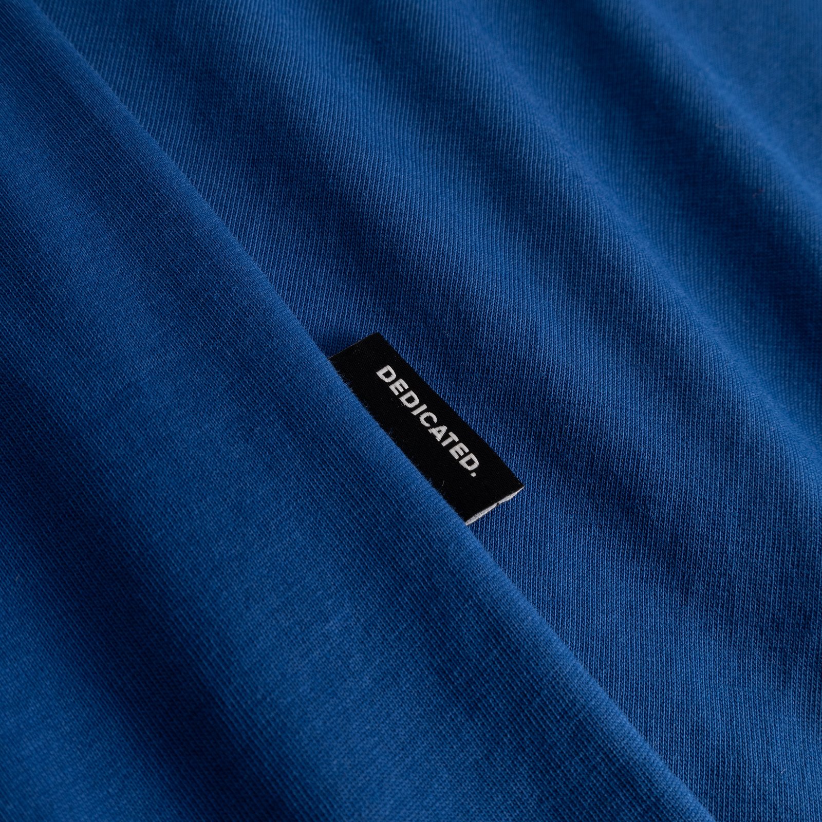 Närbild på den limogesblå T-shirten Stockholm, som visar det mjuka tyget och den svarta Dedicated-etiketten.
