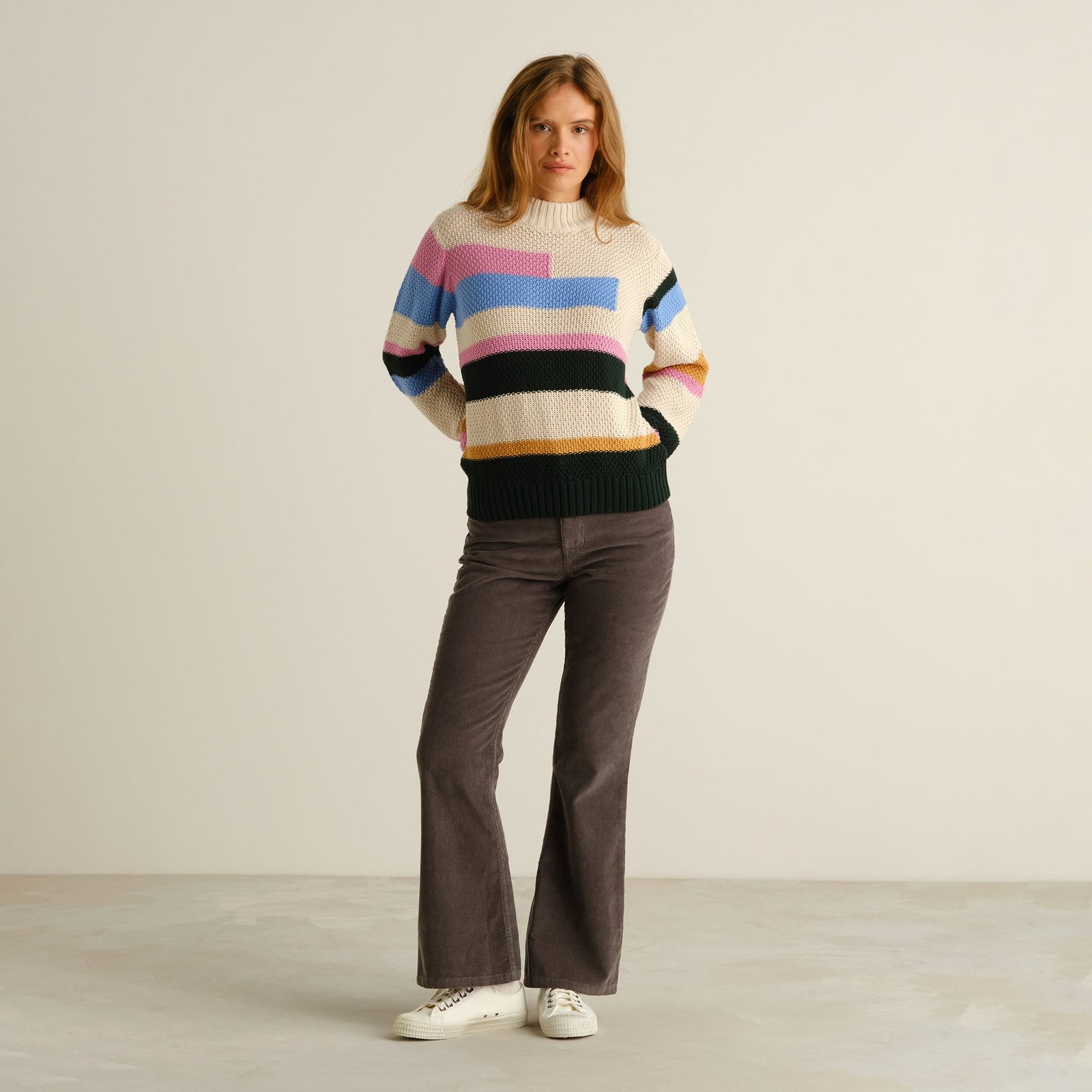 Full view of a model wearing the cozy Sweater Gotland in a fun multi-color stripe pattern with brown flared corduroys.