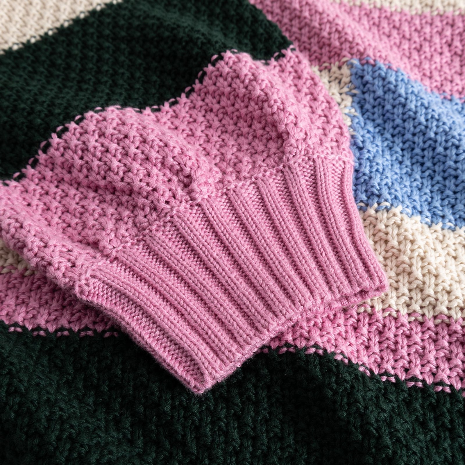 A detailed close-up of the chunky knit Sweater Gotland, highlighting the soft pink cuff and colorful striped pattern.