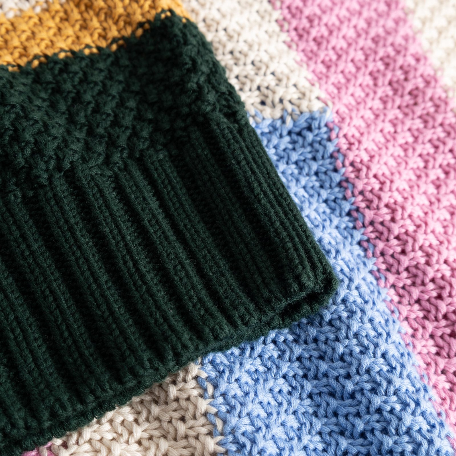 A close-up of the cozy, chunky knit of the Gotland sweater, highlighting the dark green ribbed collar and colorful stripes.
