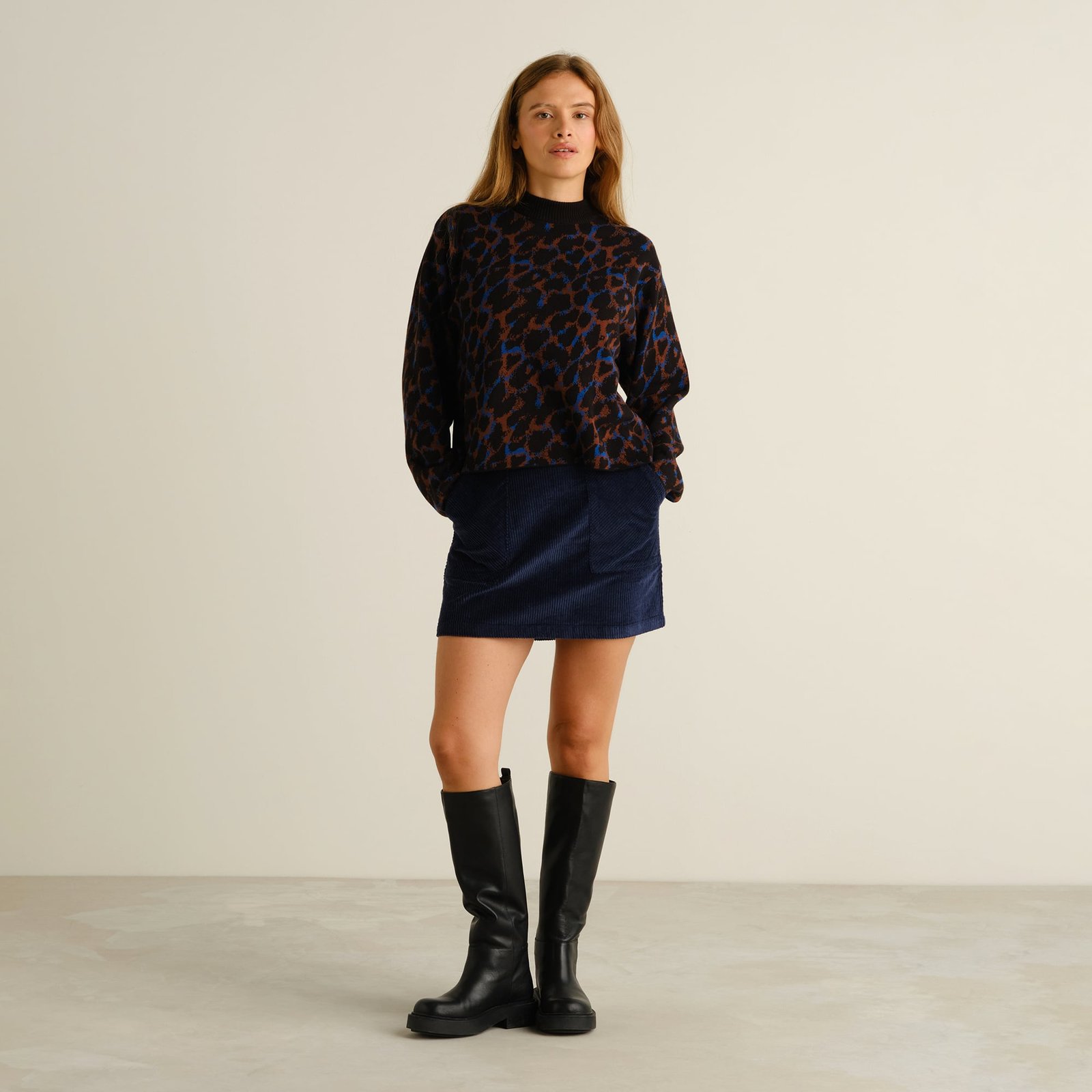Full outfit view of a model wearing the Limhamn Leopard sweater with a navy corduroy skirt and tall black boots.