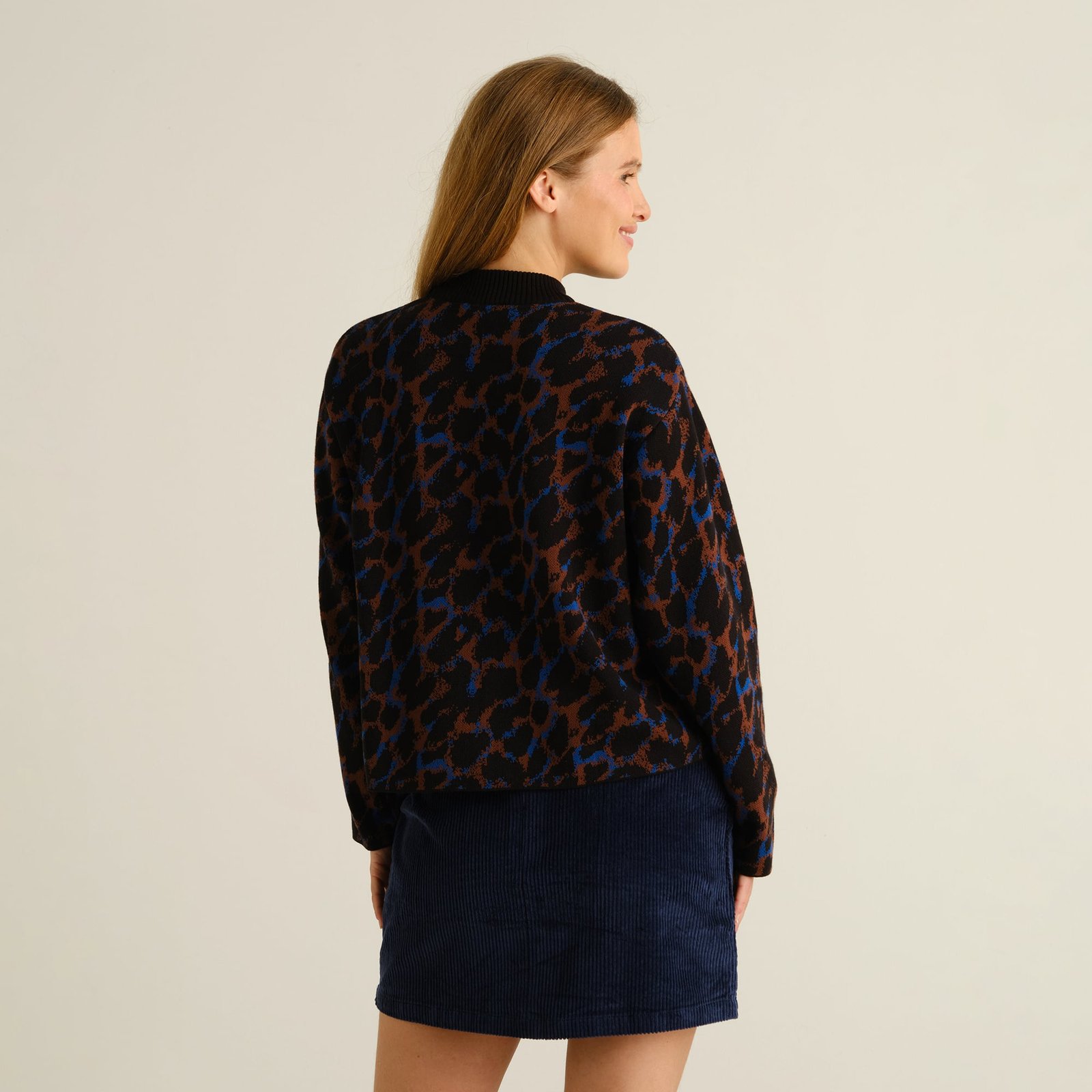 A woman looks over her shoulder, showing off the back of the cozy Limhamn sweater in a cool multi-colored leopard print.
