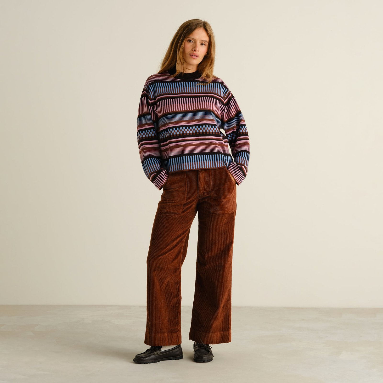 Full outfit view of a model wearing the multi-colored Limhamn sweater with brown corduroy pants and black loafers.