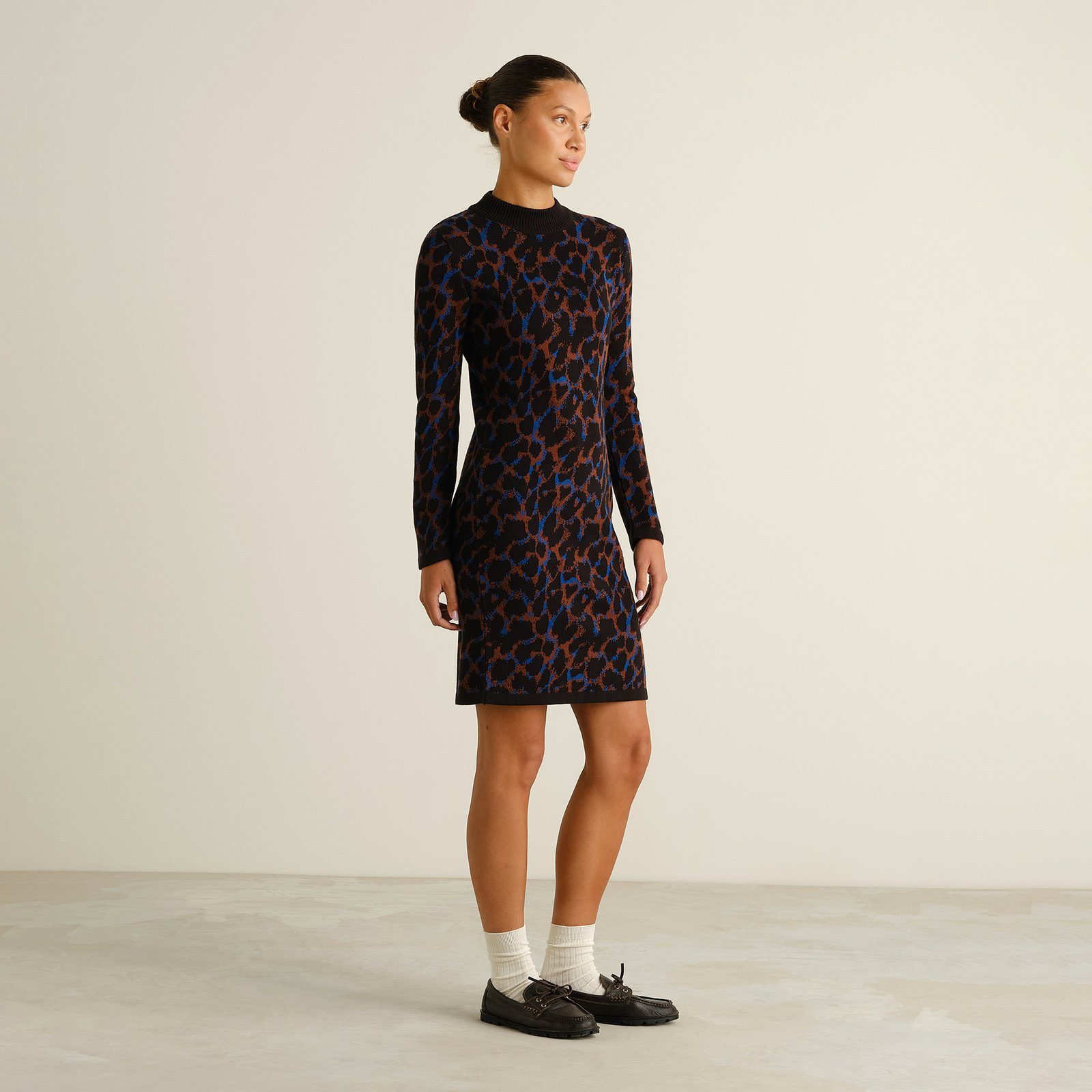 Seitenansicht eines Models, das das Strickkleid Lo Leopard Multi Color zu Loafern und weißen Socken trägt.