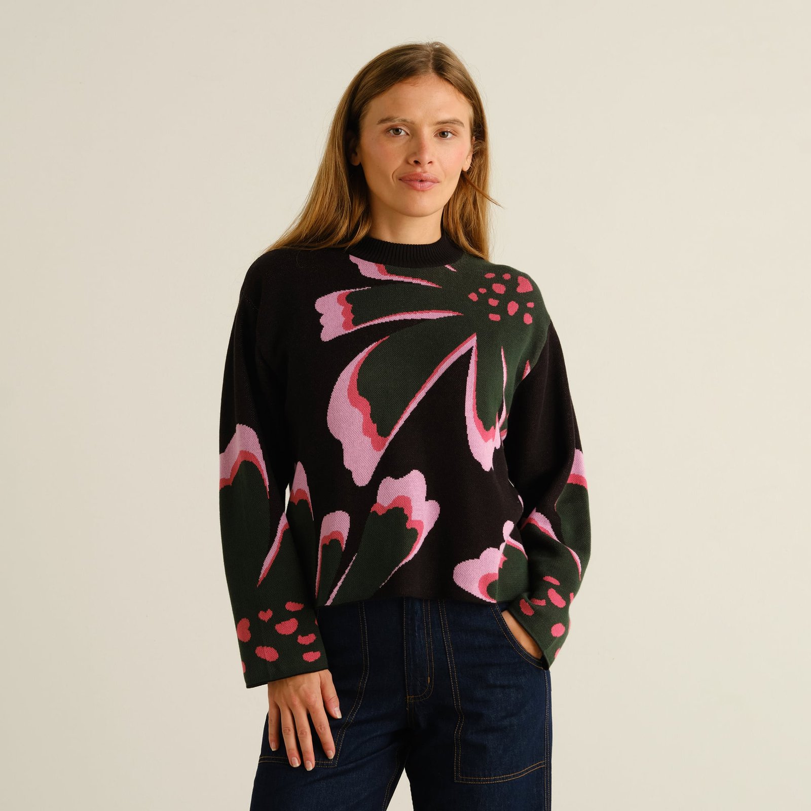 A model wears the Sweater Limhamn Big Bloom, a black jacquard knit with a bold floral pattern in pink and dark green.