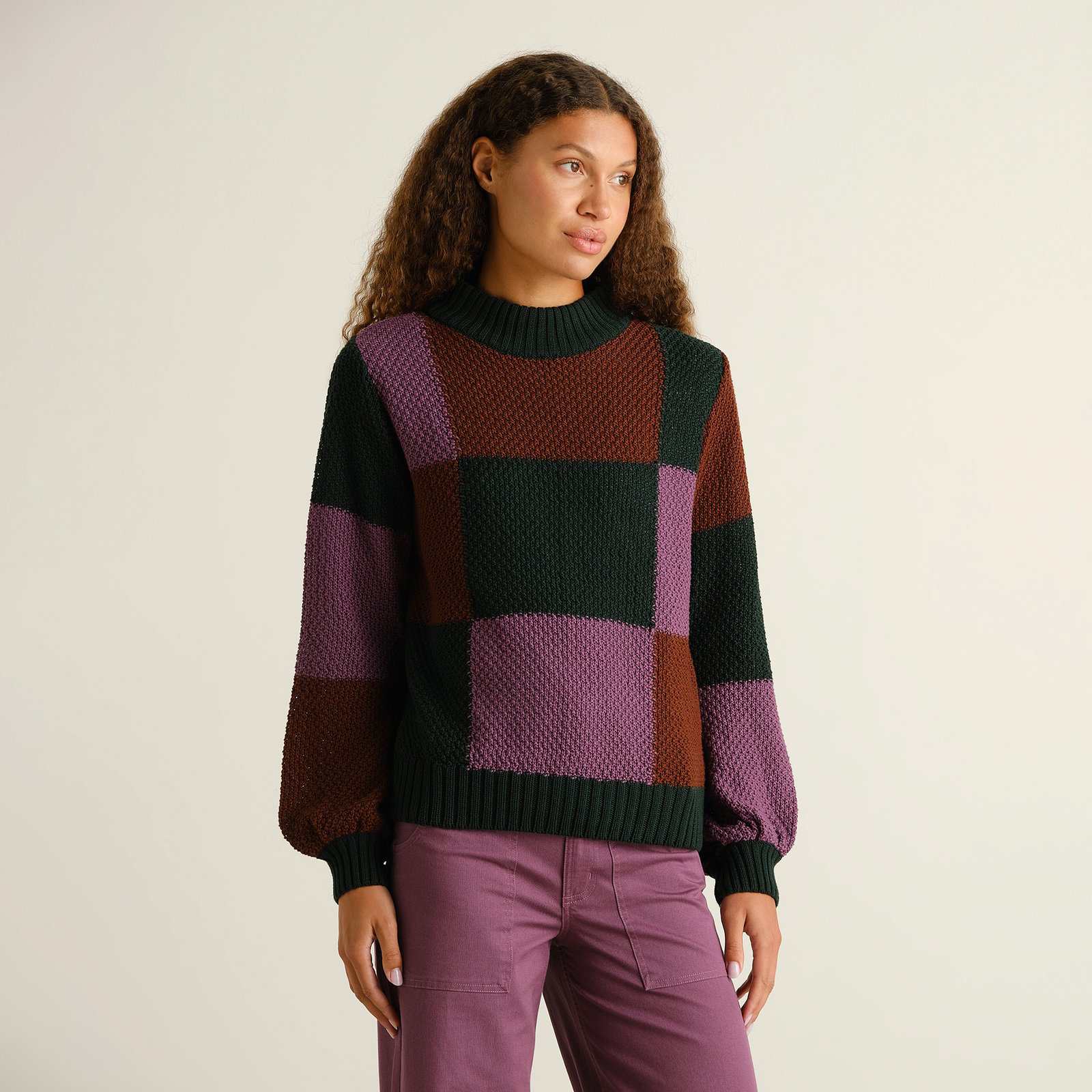 Model wearing the Gotland Sweater in a multi-colored blocked check pattern. The chunky knit has a high neck and relaxed fit.