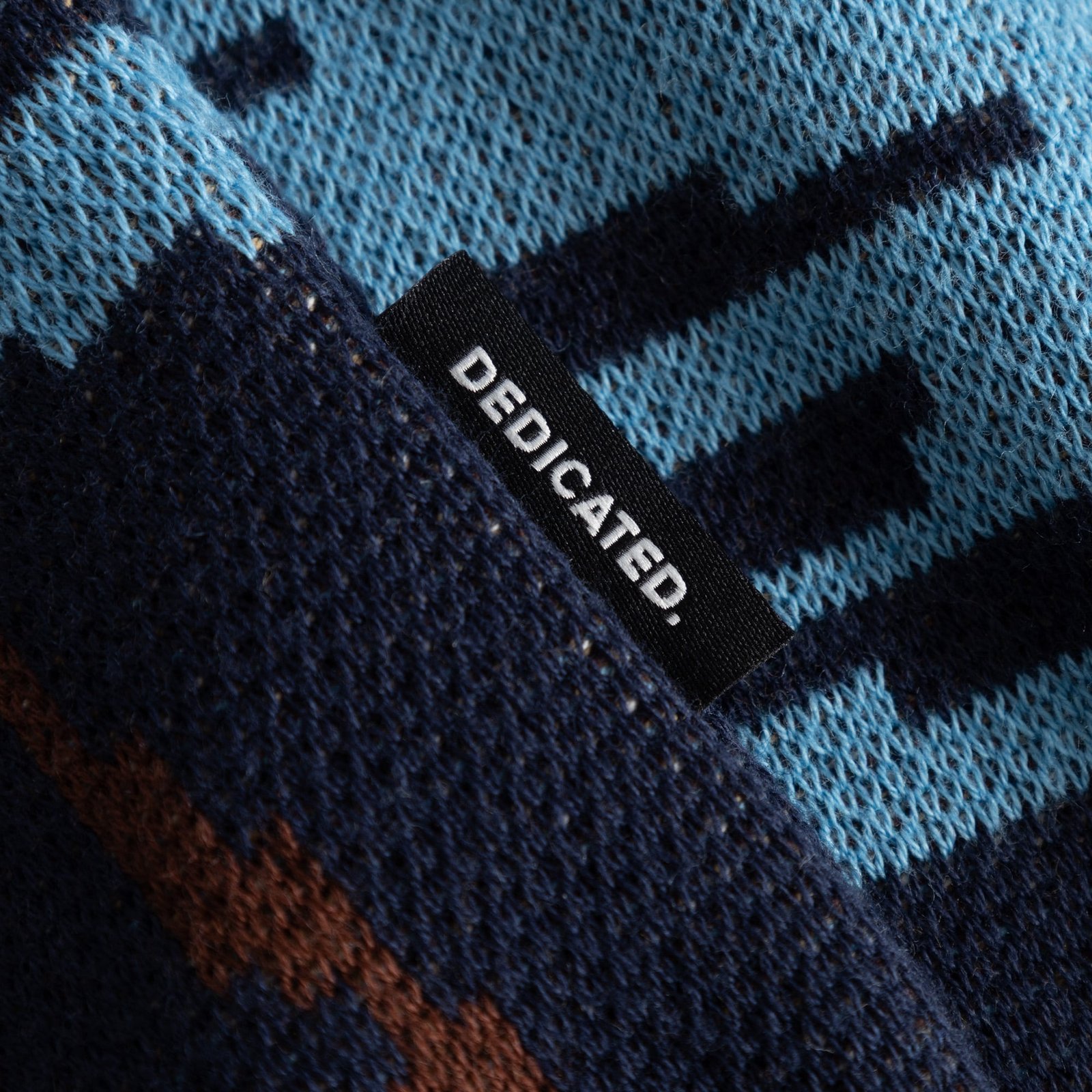 Close-up of the jacquard-knit Sweater Mora in blue and brown, showing the Dedicated brand label sewn on the side.