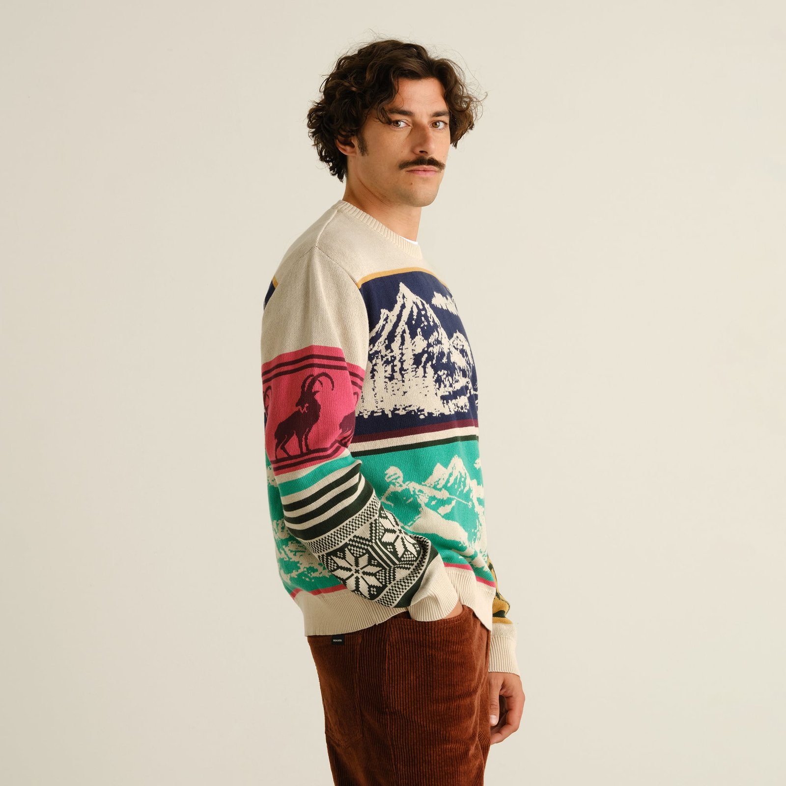 A model with a mustache wears the Sweater Mora Retro Ski Blocks, a colorful knit with a fun, vintage ski-inspired pattern.
