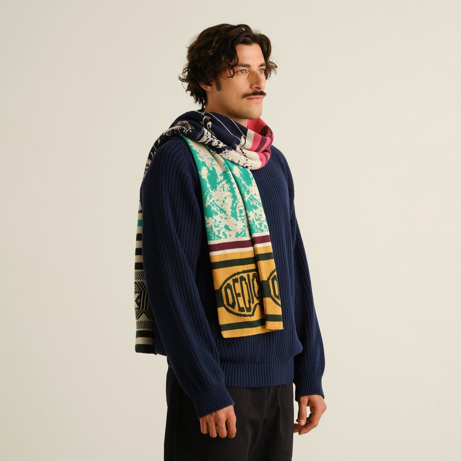 Male model in a studio setting, wearing a navy blue sweater and the vibrant, multi-colored Rossberga Retro Ski scarf.