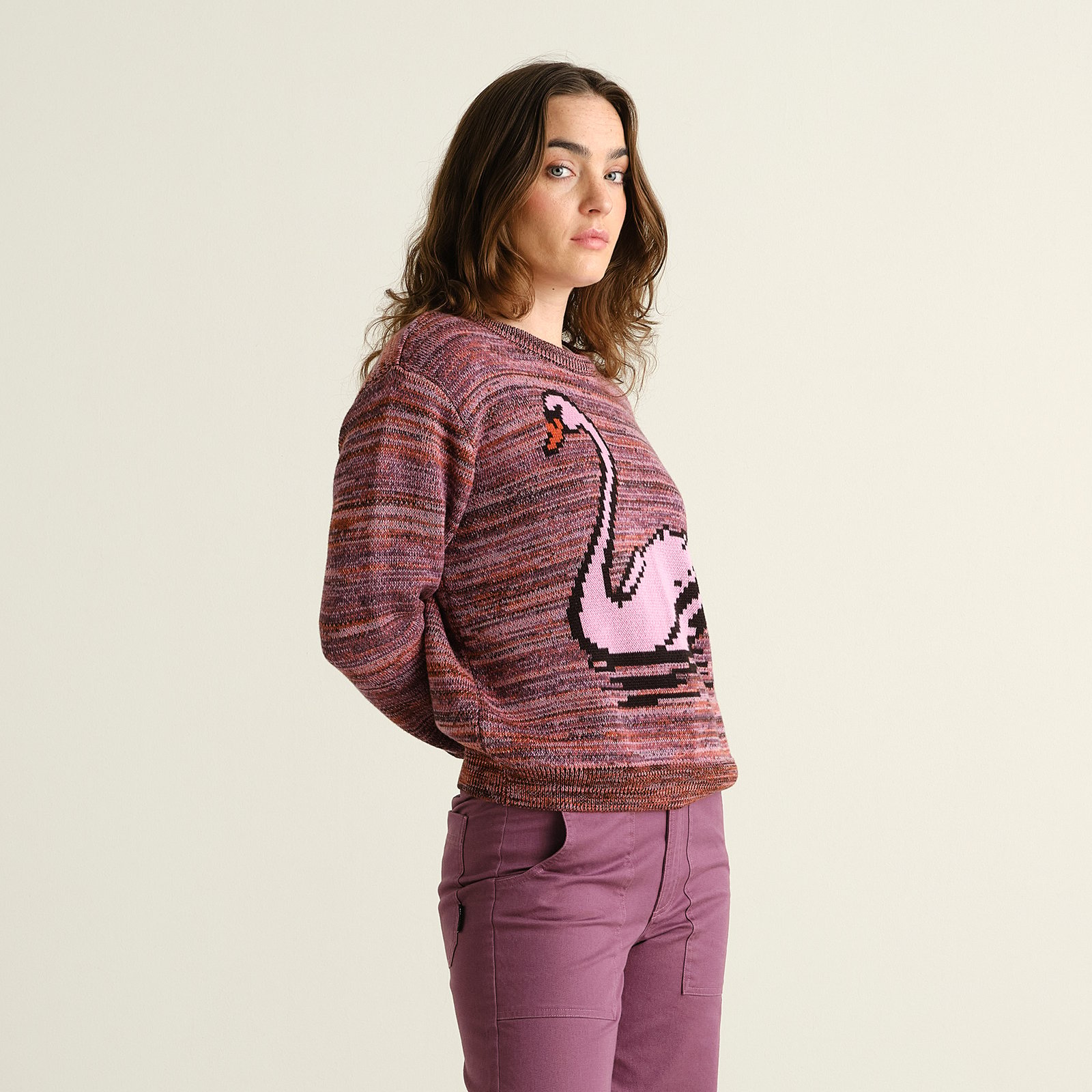 A woman looks over her shoulder, showing off the fun pixelated swan design on the multi-colored Arendal knit sweater.