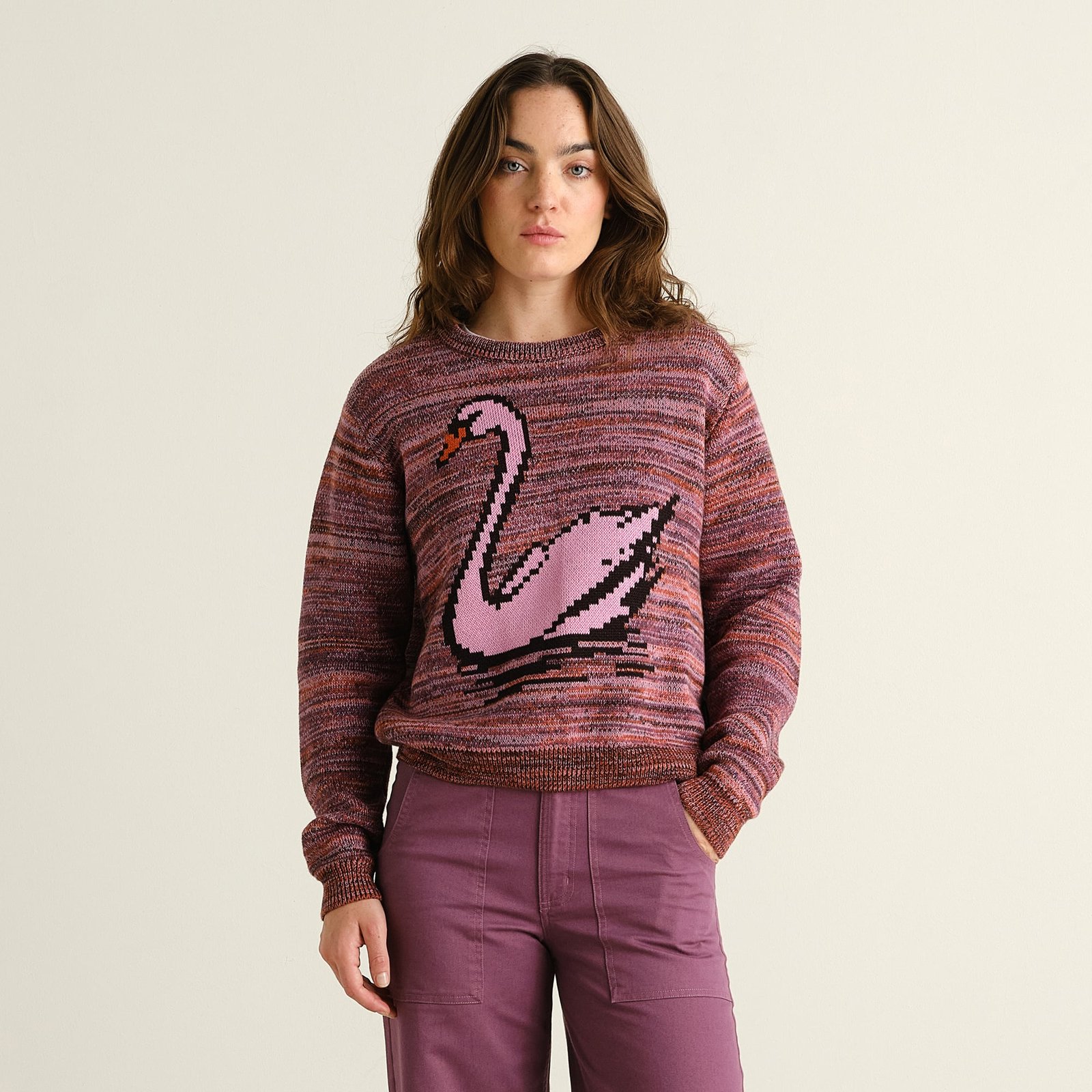 Model wears the cozy Arendal sweater in a multi-color knit, featuring a playful pixelated pink swan.