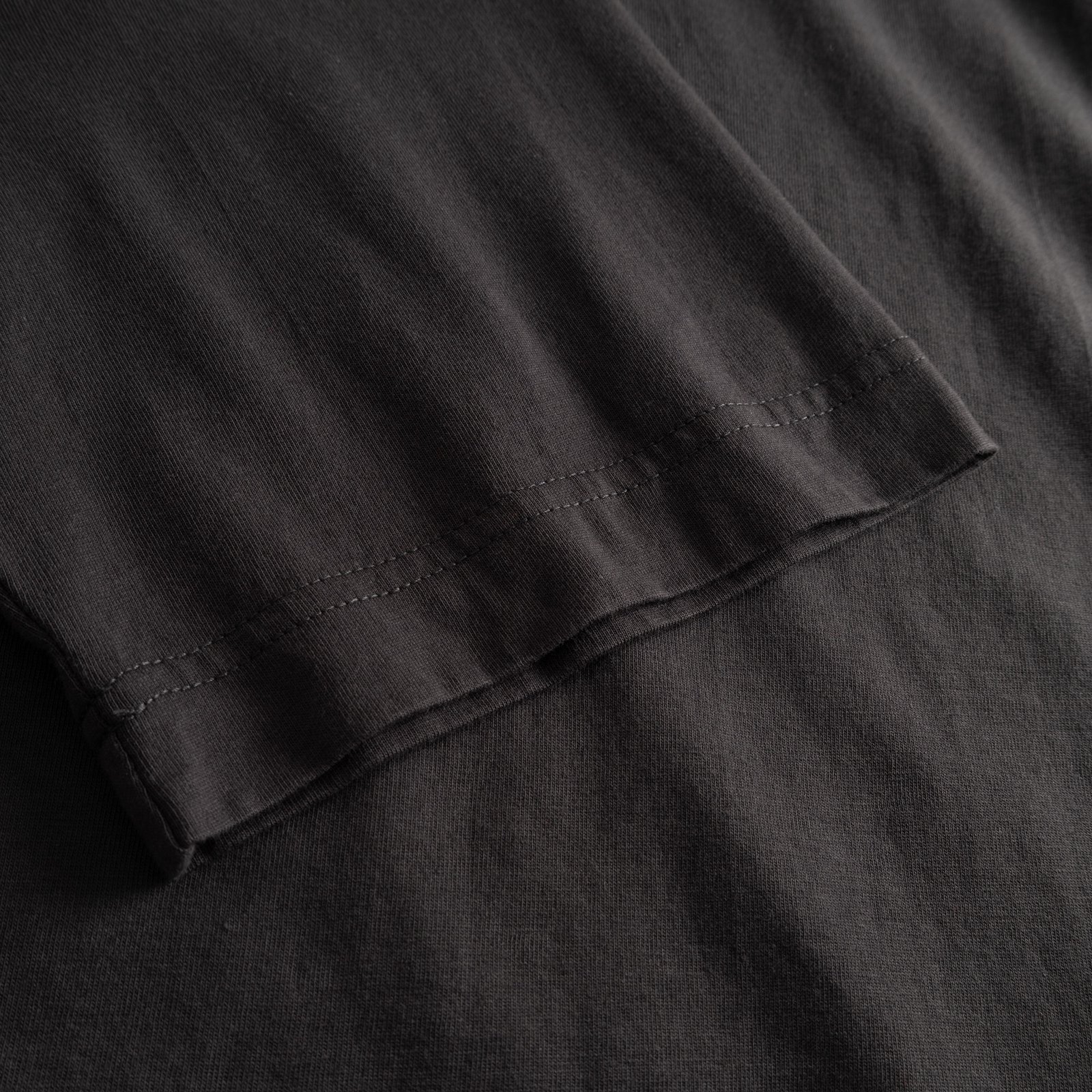 A close-up of the charcoal T-shirt Vadstena, highlighting the detailed stitching on the sleeve.