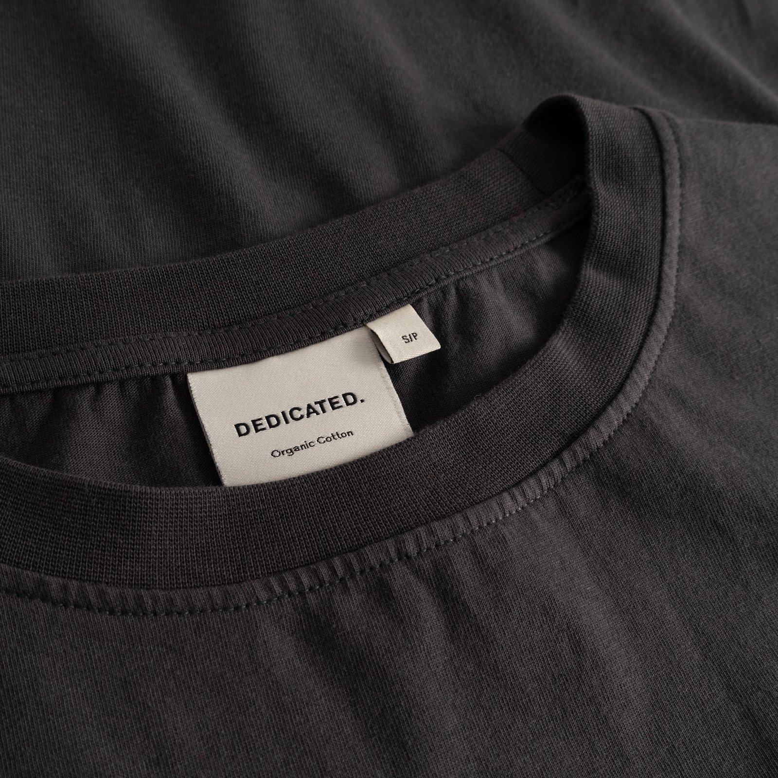 Detail shot of the Dedicated brand label inside the soft, ribbed collar of the charcoal T-shirt Vadstena.