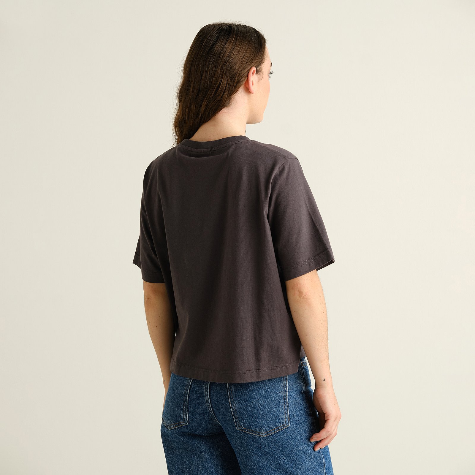 Back view of a model wearing the T-shirt Vadstena Screaming Cat in charcoal, showing its relaxed fit with blue jeans.