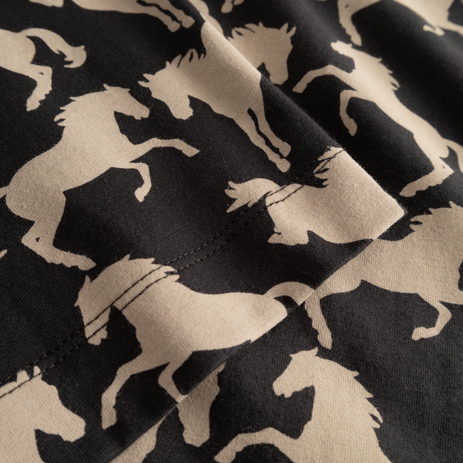 Close-up detail of the T-shirt Vadstena, showcasing the wild horses all-over print on the charcoal organic cotton fabric.