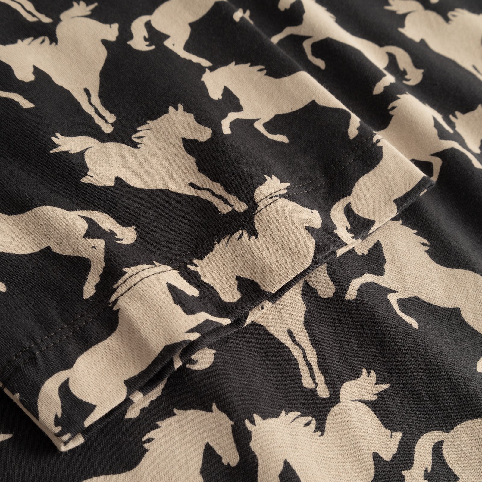 Close-up of the sleeve on the T-shirt Vadstena, showing the all-over wild horses print on charcoal fabric.