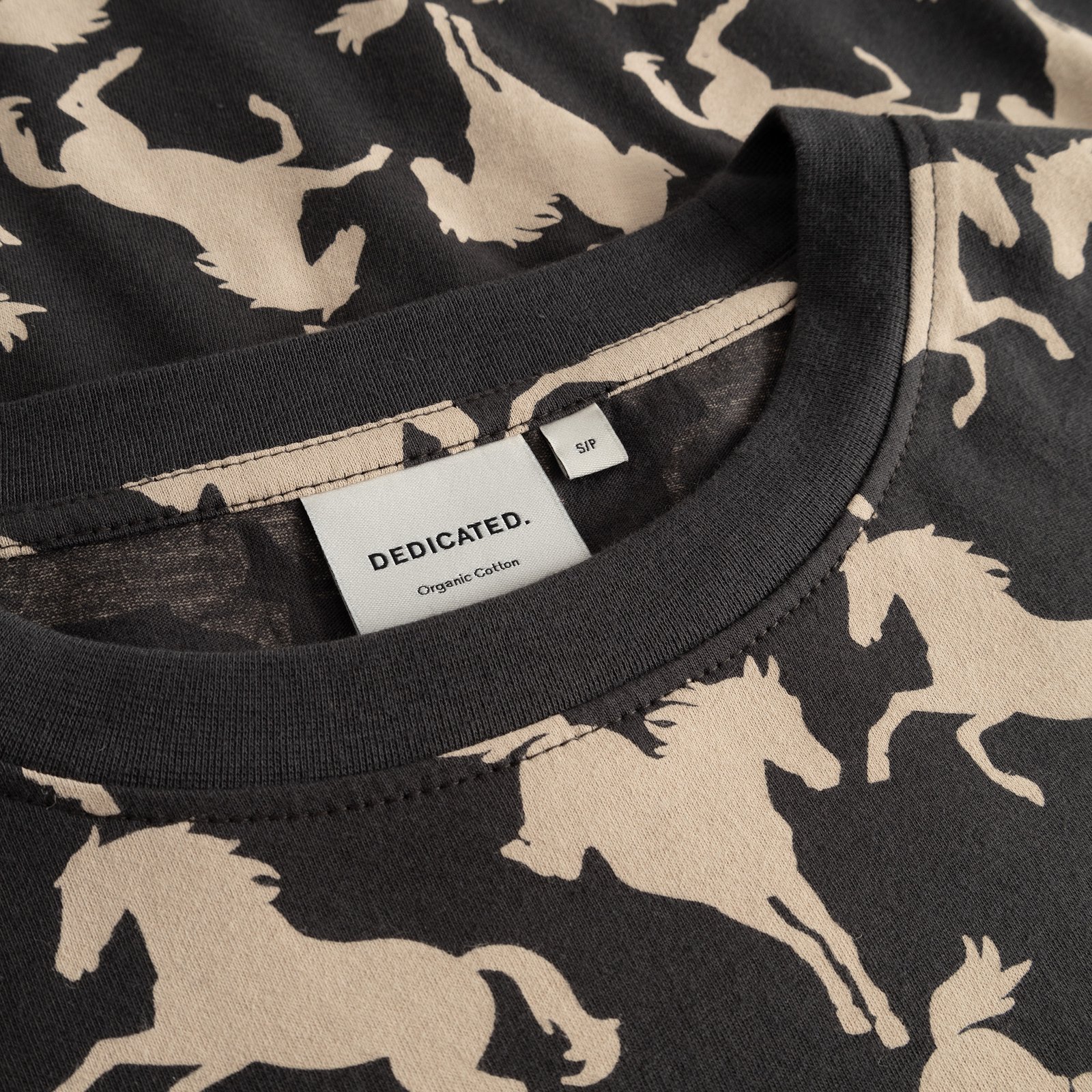 A close-up view of the collar on the charcoal T-shirt Vadstena with its all-over wild horses print and the Dedicated label.