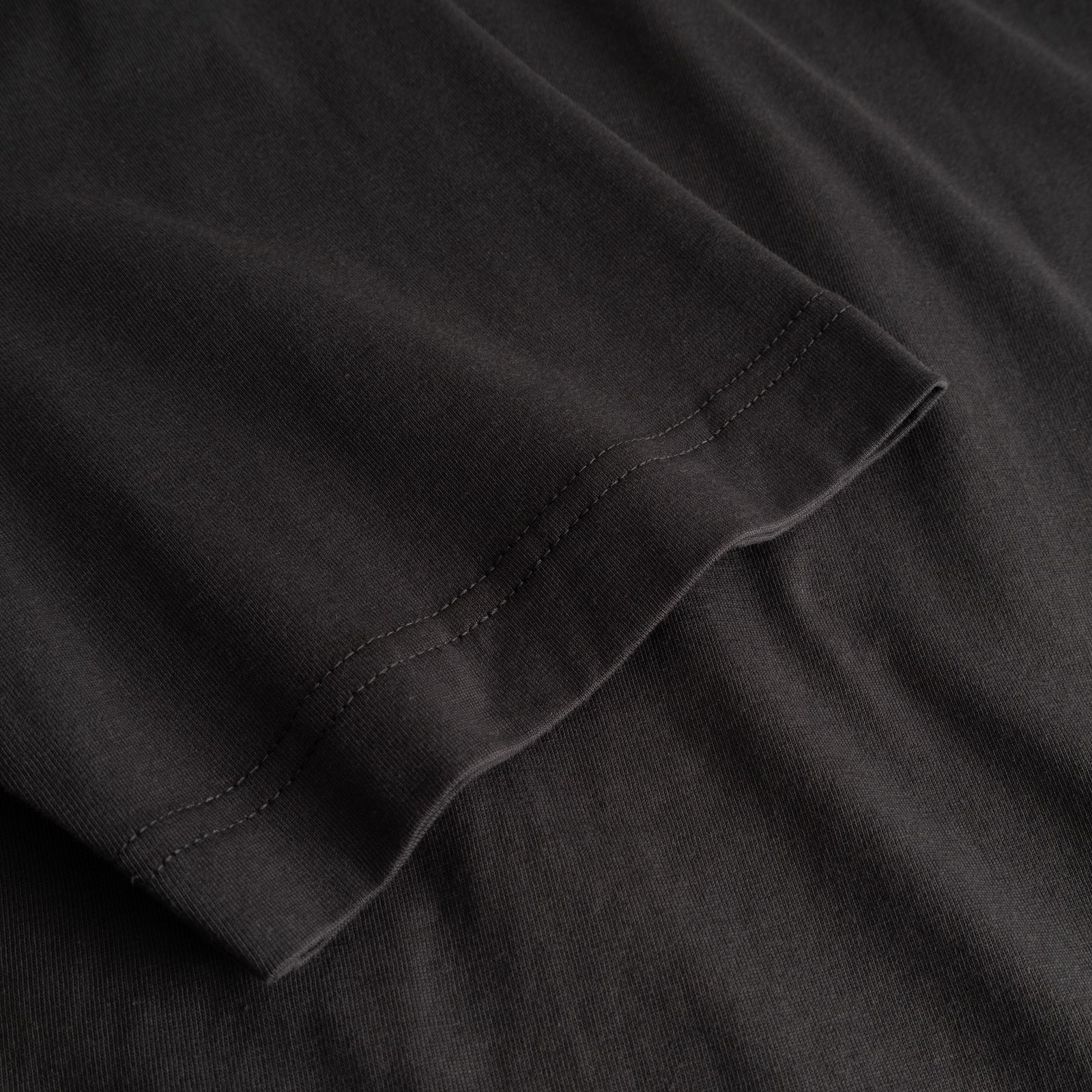 A close-up of the charcoal T-shirt Vadstena, showing the fine stitching detail on the sleeve.