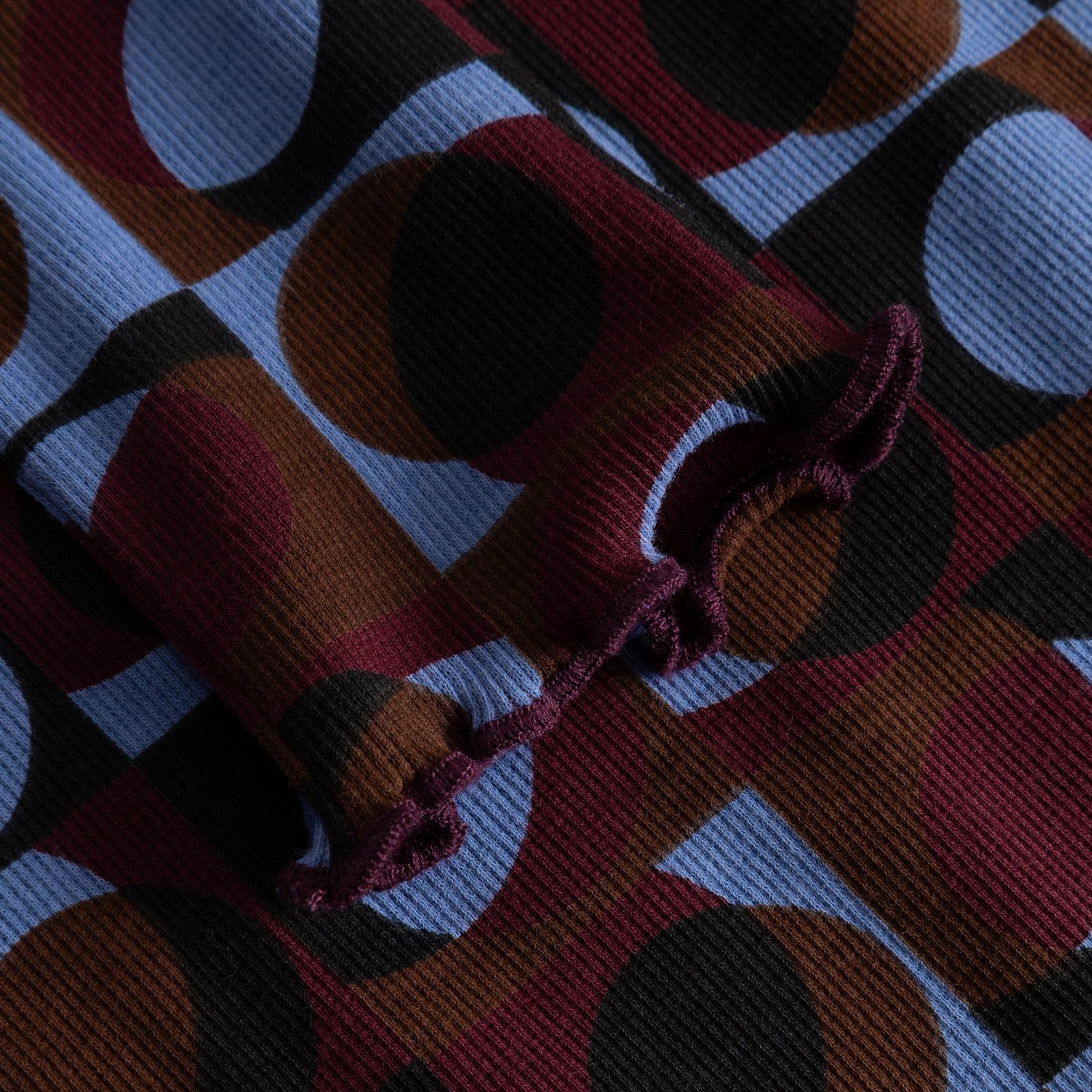 Close-up of the lettuce-edge cuff on the Rib Top Ryd, showing the vibrant retro geometric print and ribbed texture.