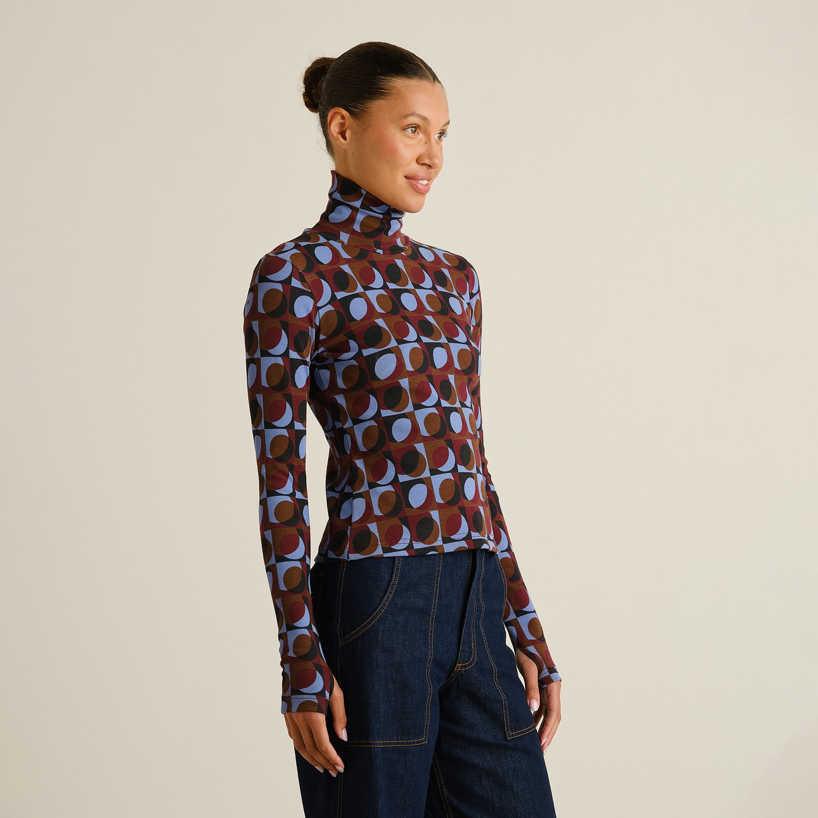 A smiling woman models the slim-fit Rib Top Malma in a fun Retro Geo Multi Color print, paired with dark wash jeans.
