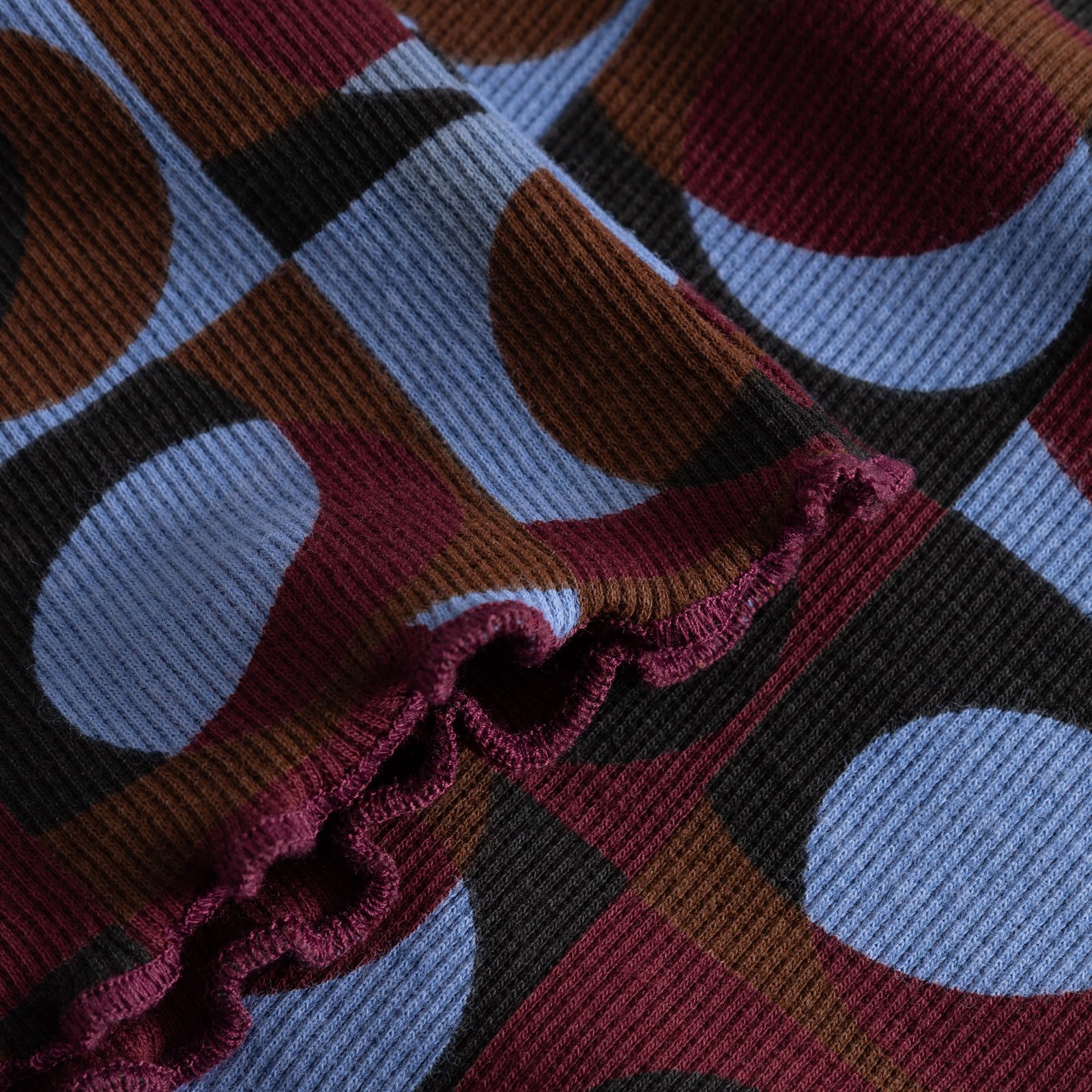 A close-up of the ribbed fabric of the Dress Lofta, showing the Retro Geo print and delicate lettuce seam detail.