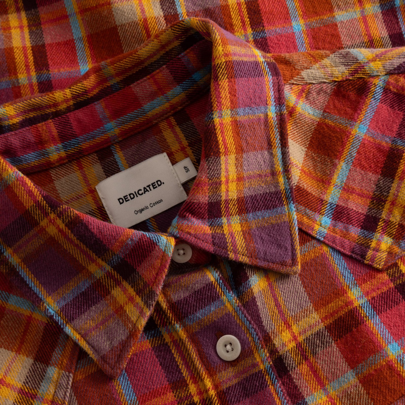 A close-up view of the cozy Arboga Flannel Shirt, highlighting its rich multi-color madras check and the Dedicated label.