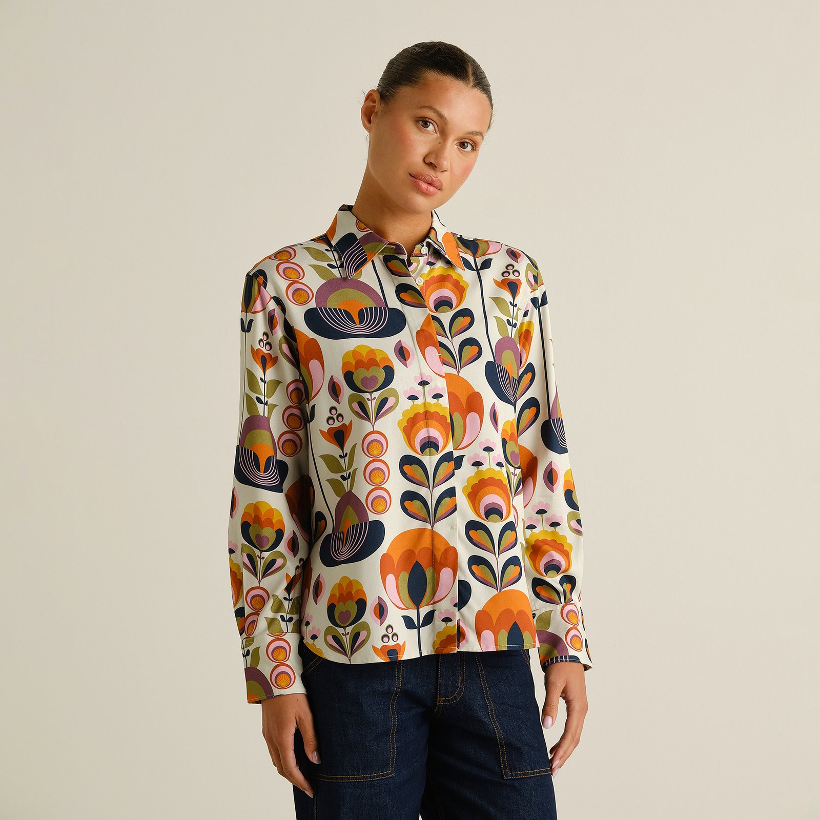 Kvinna i skjortan Nydalen med det färgstarka, blommiga retromönstret Autumn Harvest, stylad med mörka jeans.