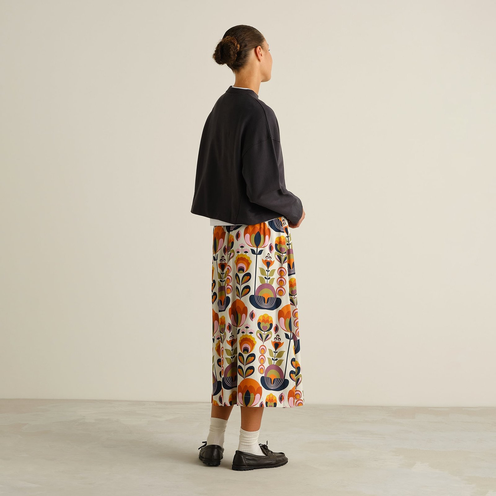 Back view of model wearing the Skirt Viken in Autumn Harvest print, styled with a dark cropped sweater and loafers.