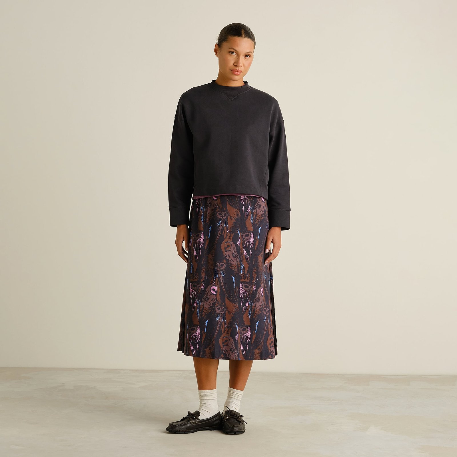 Model wearing the multi-colored Viken skirt with an owl print, styled with a black sweatshirt, white socks and black loafers.
