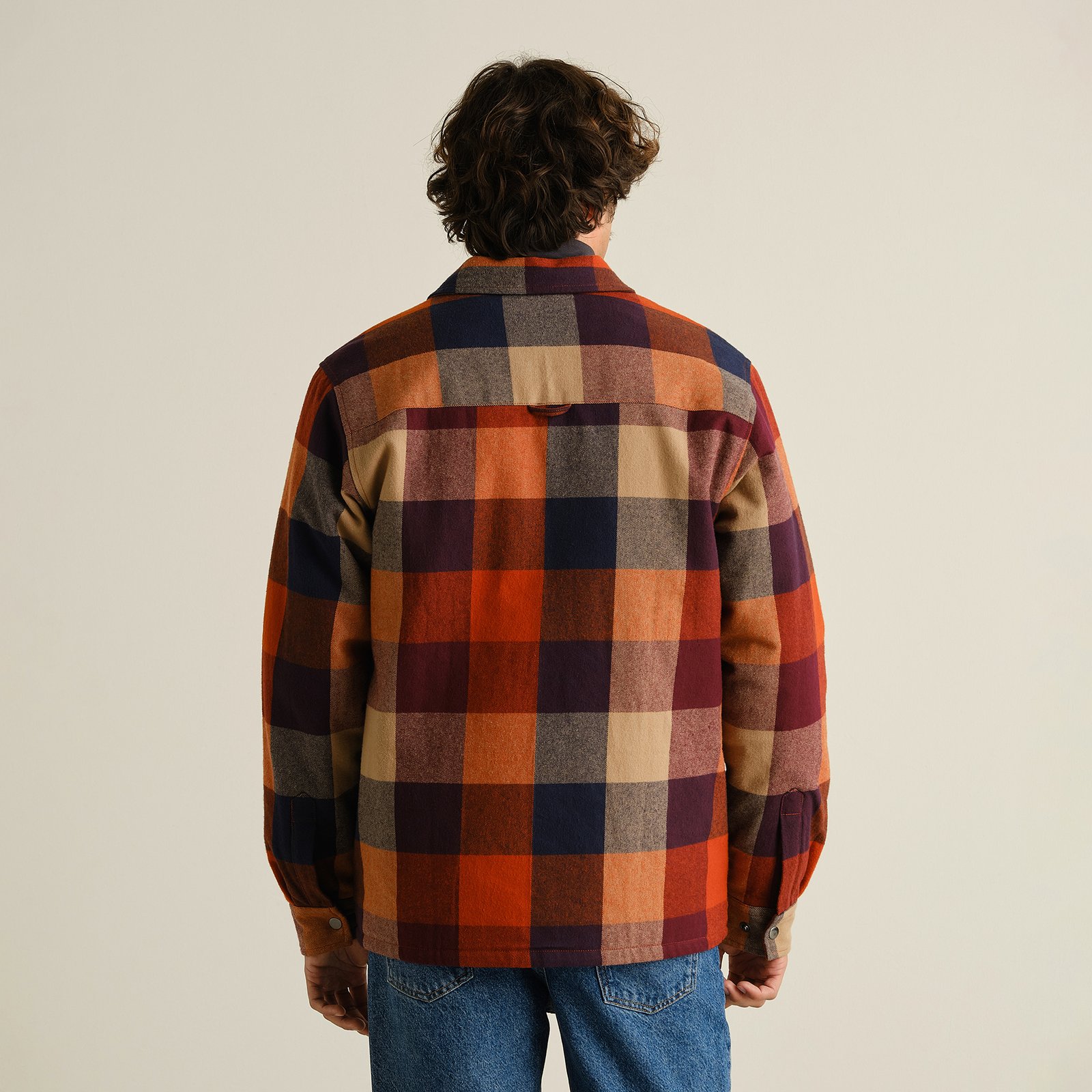 Back view of a male model wearing the muted multi-color Jacket Torp Flannel Check over blue jeans in a studio setting.