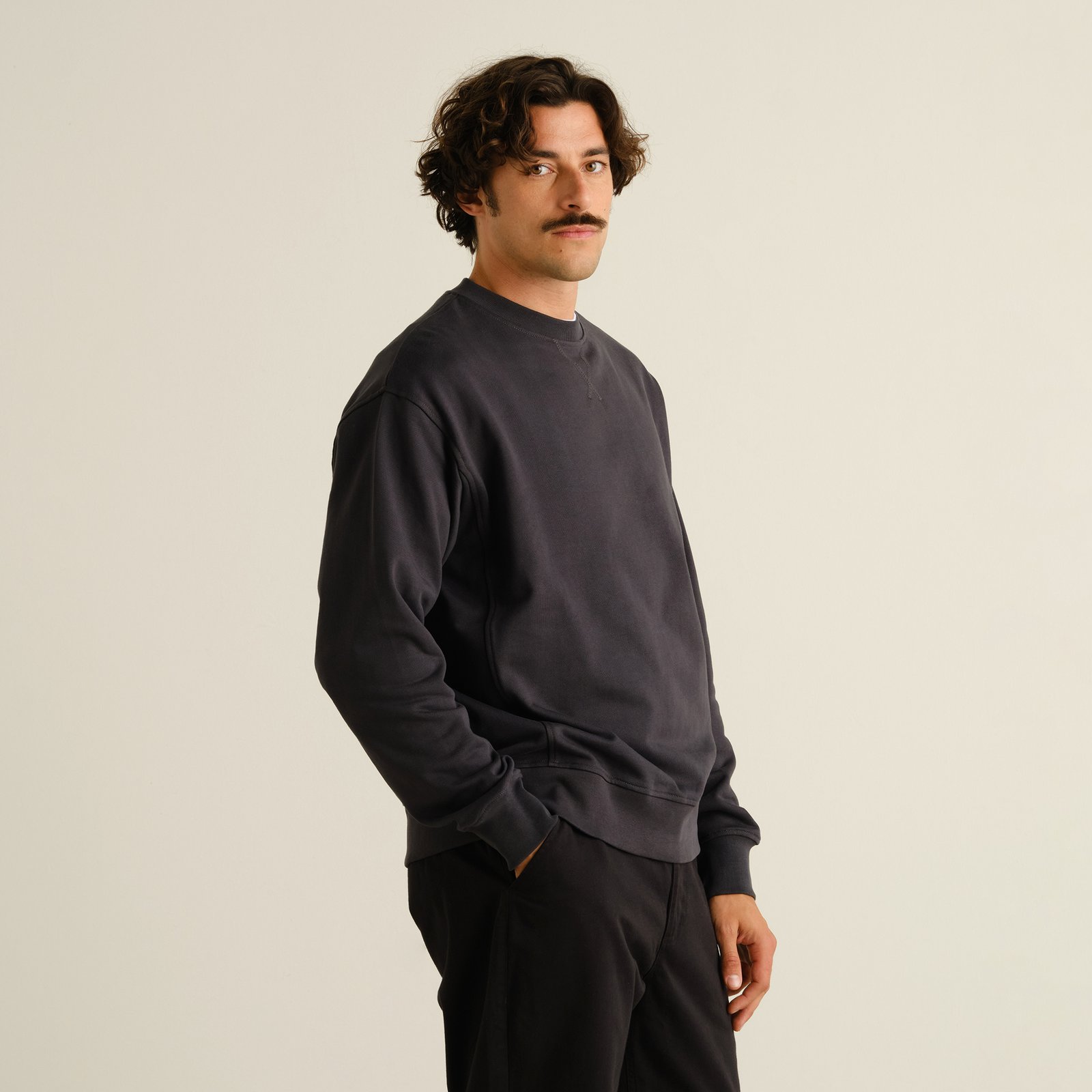 A male model with a mustache wears the relaxed-fit Bettna sweatshirt in Phantom Black against a simple studio background.