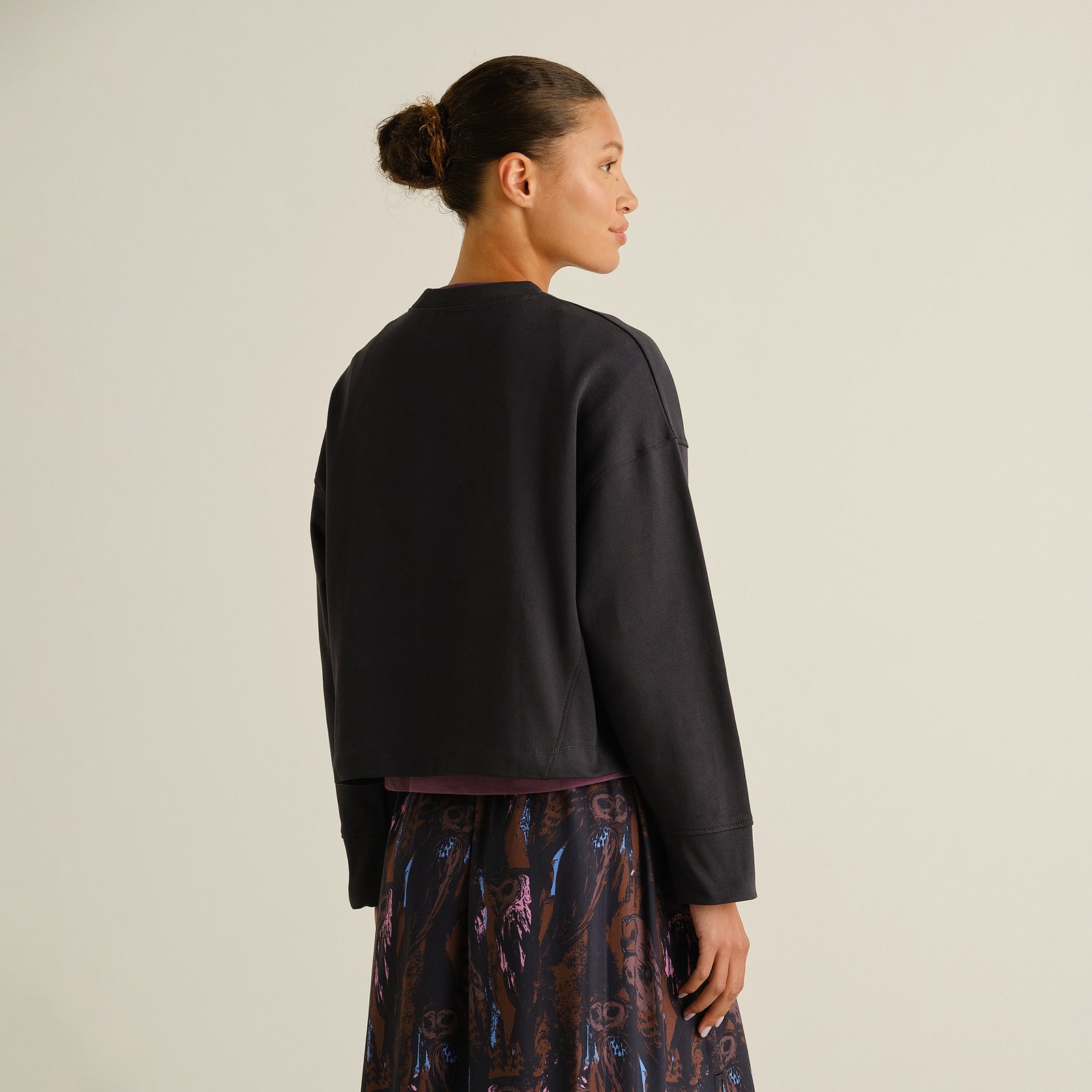 A model shows the back of the relaxed-fit Sweatshirt Gia Phantom Black, styled with a patterned skirt.