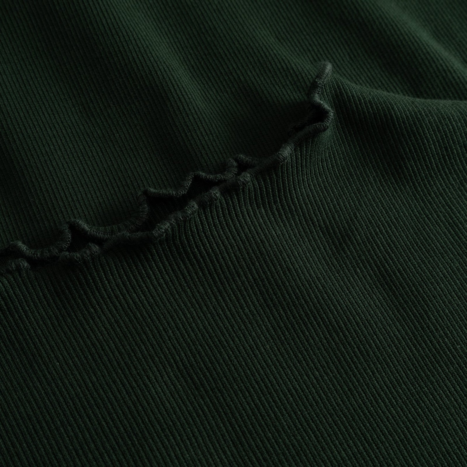 Close-up detail shot of the Rib Dress Lofta in dark green, showing the soft ribbed fabric and delicate lettuce seam.