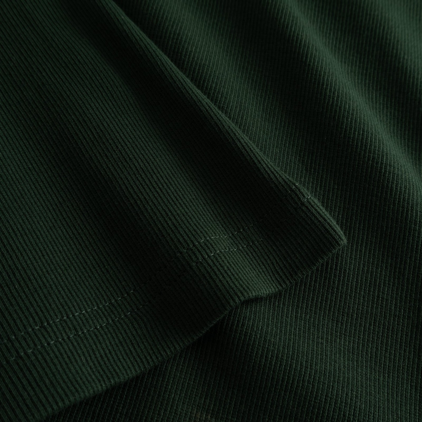 A close-up shot of the rich dark green ribbed fabric and sleeve hem detail of the Malma Top.