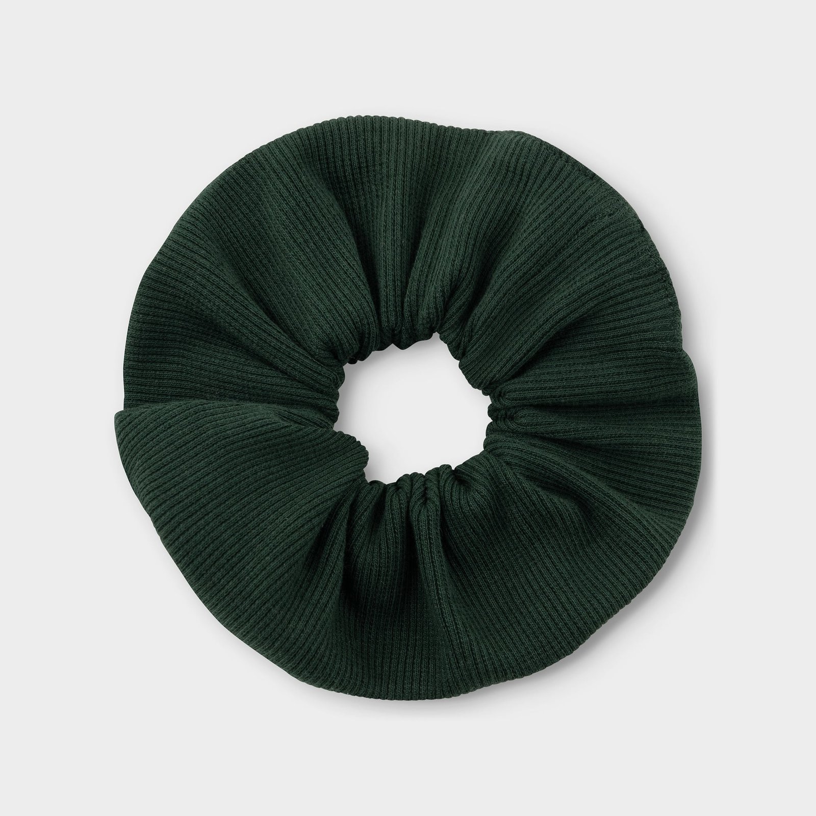 A dark green scrunchie with a ribbed texture, seen from above on a light background.