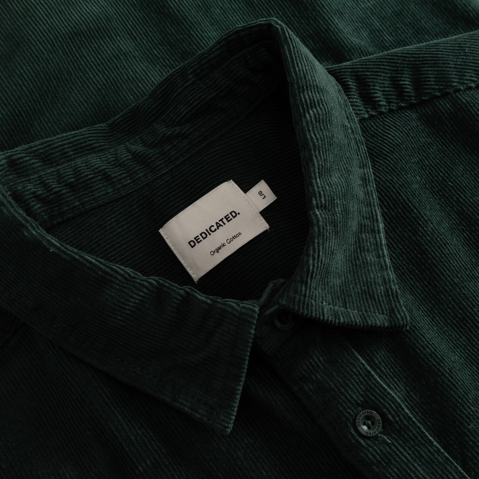 A close-up studio shot of the Dedicated brand label inside the collar of the dark green corduroy shirt Varberg.