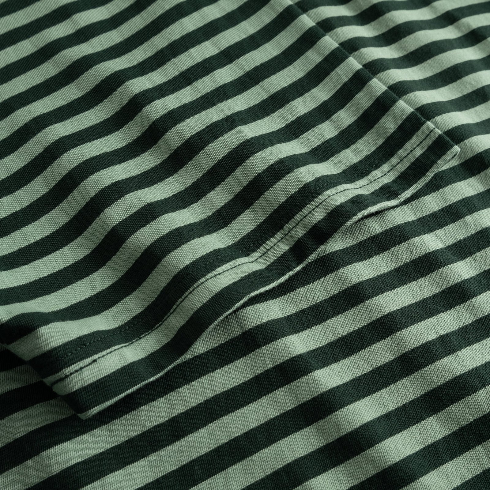 Detailed shot of the organic cotton fabric of the Stockholm T-shirt in a dark green and granite green striped pattern.