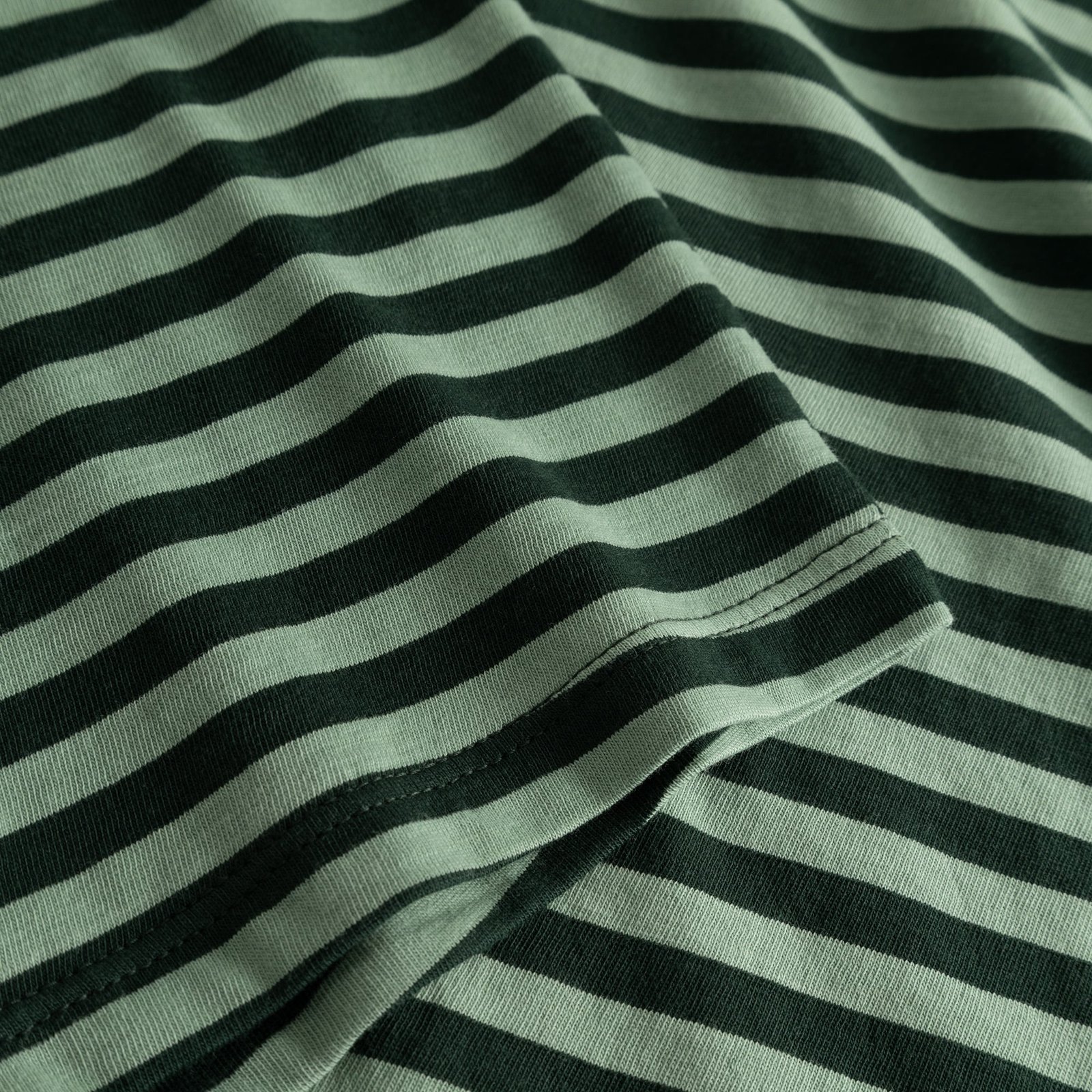 Close-up of the Top Humledal's soft jersey fabric, featuring dark green and granite green stripes and sleeve hem detail.