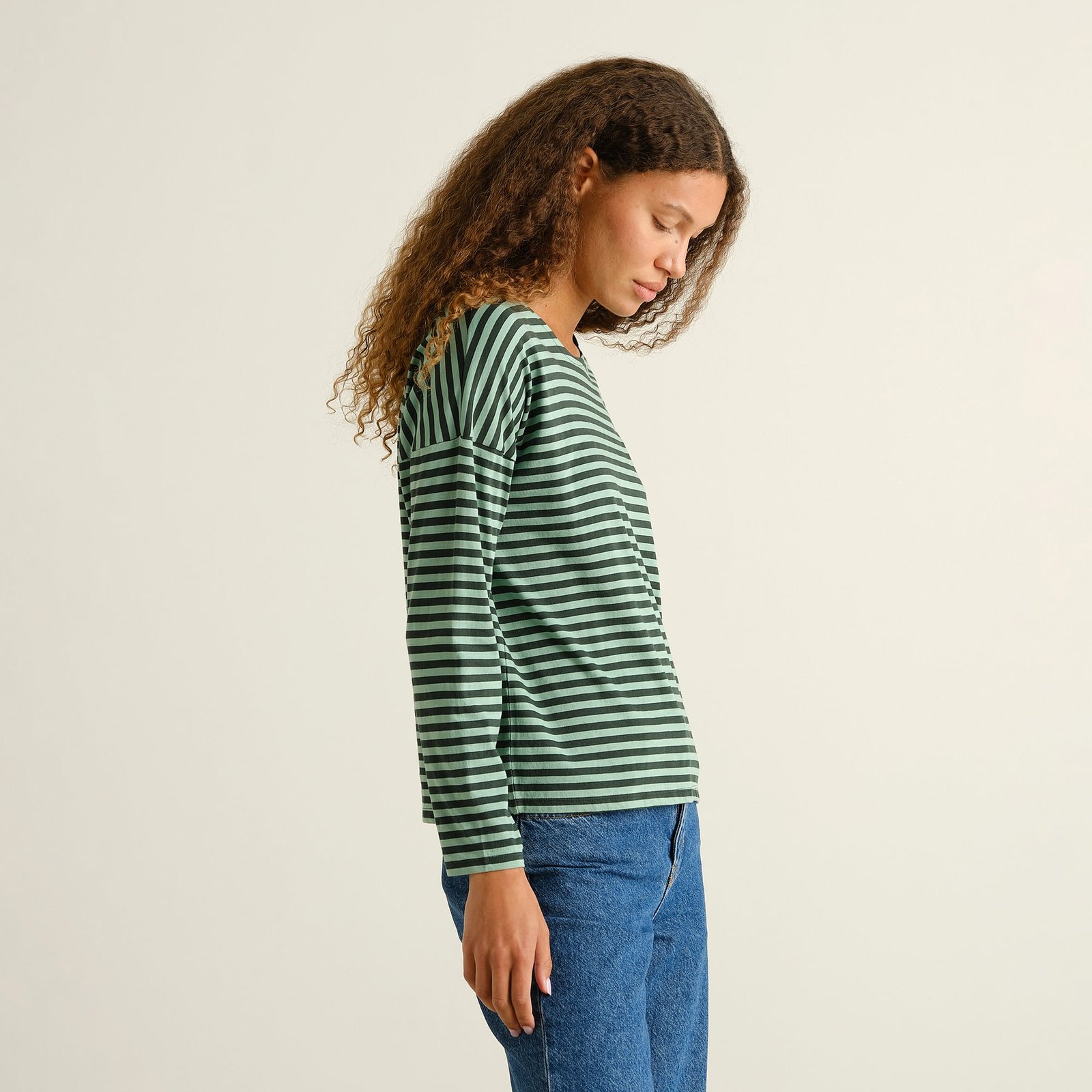 A woman shows off the relaxed, boxy fit of the striped green Humledal top, styled casually with a pair of blue jeans.