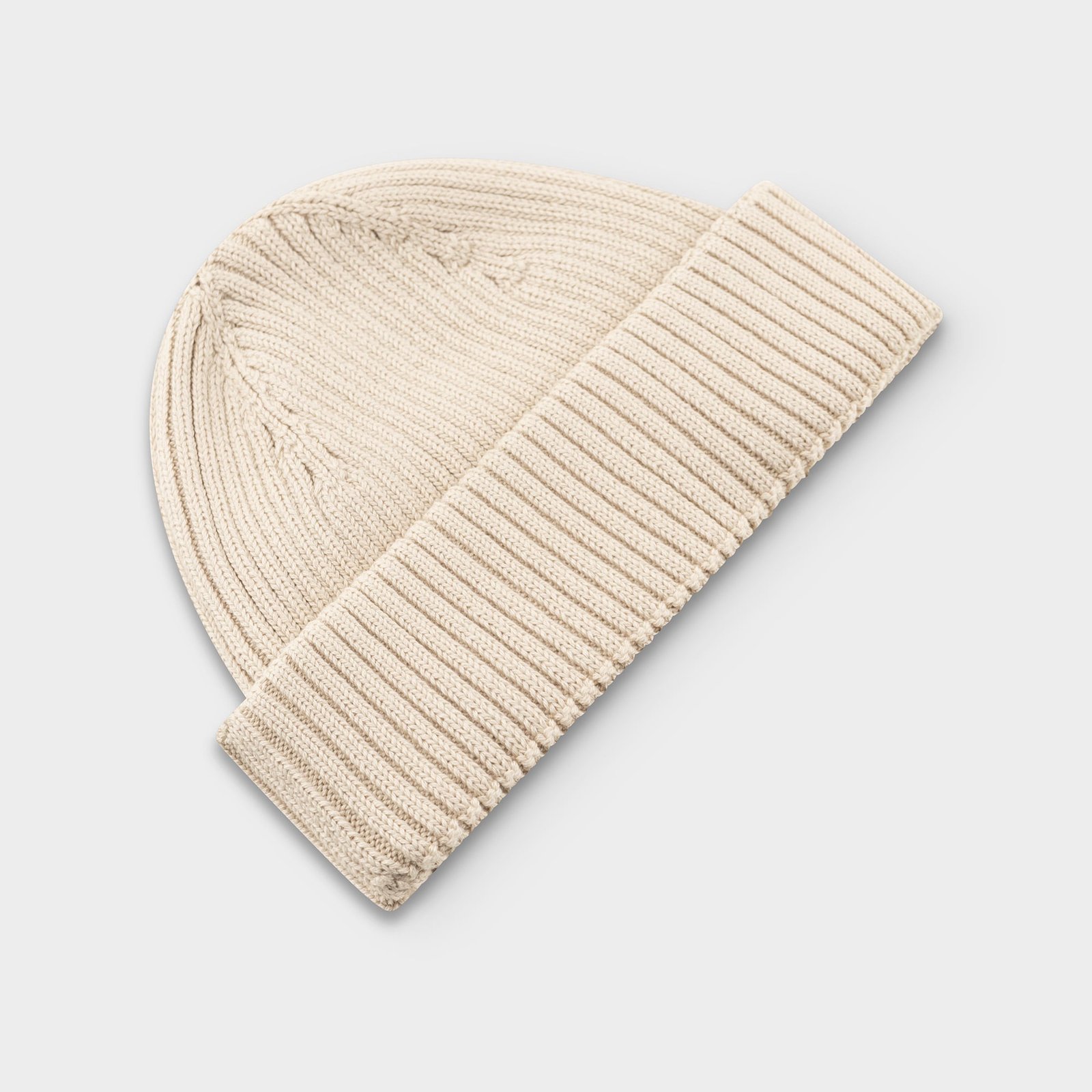 The Rutvik Beanie in a soft Oat White color, shown laid flat in a studio shot to highlight its classic rib-knit design.