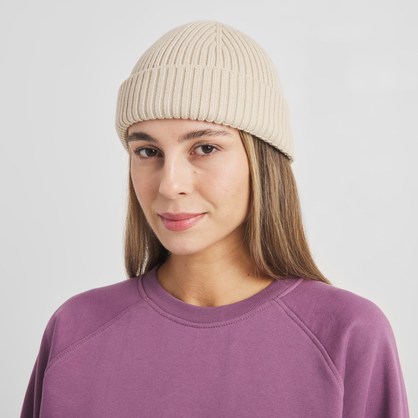 A close-up of a woman wearing the short, ribbed-knit Beanie Rutvik in Oat White against a light studio background.