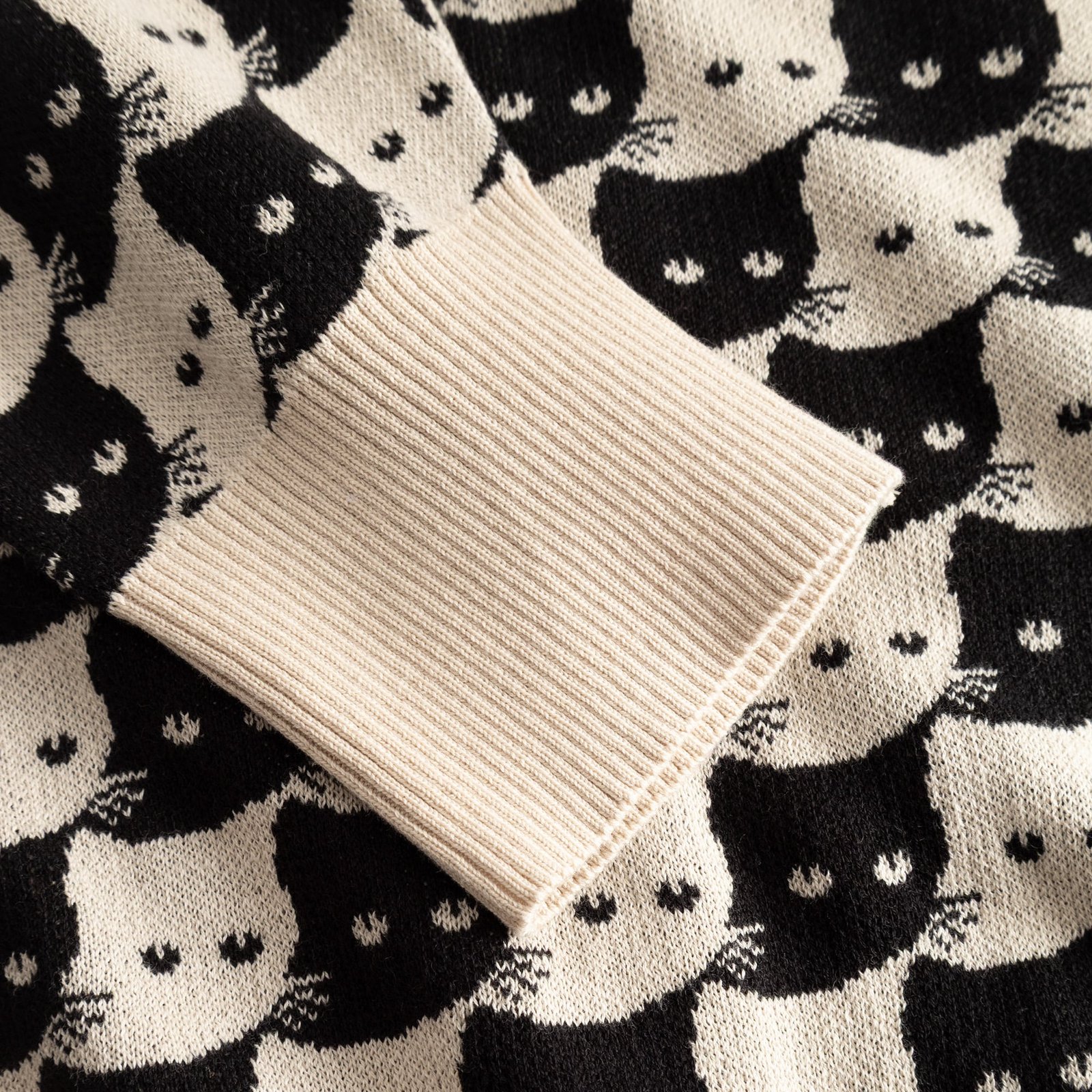 Close-up of the oat white ribbed cuff on the Cardigan Kanan, set against the playful black and white jacquard cat pattern.