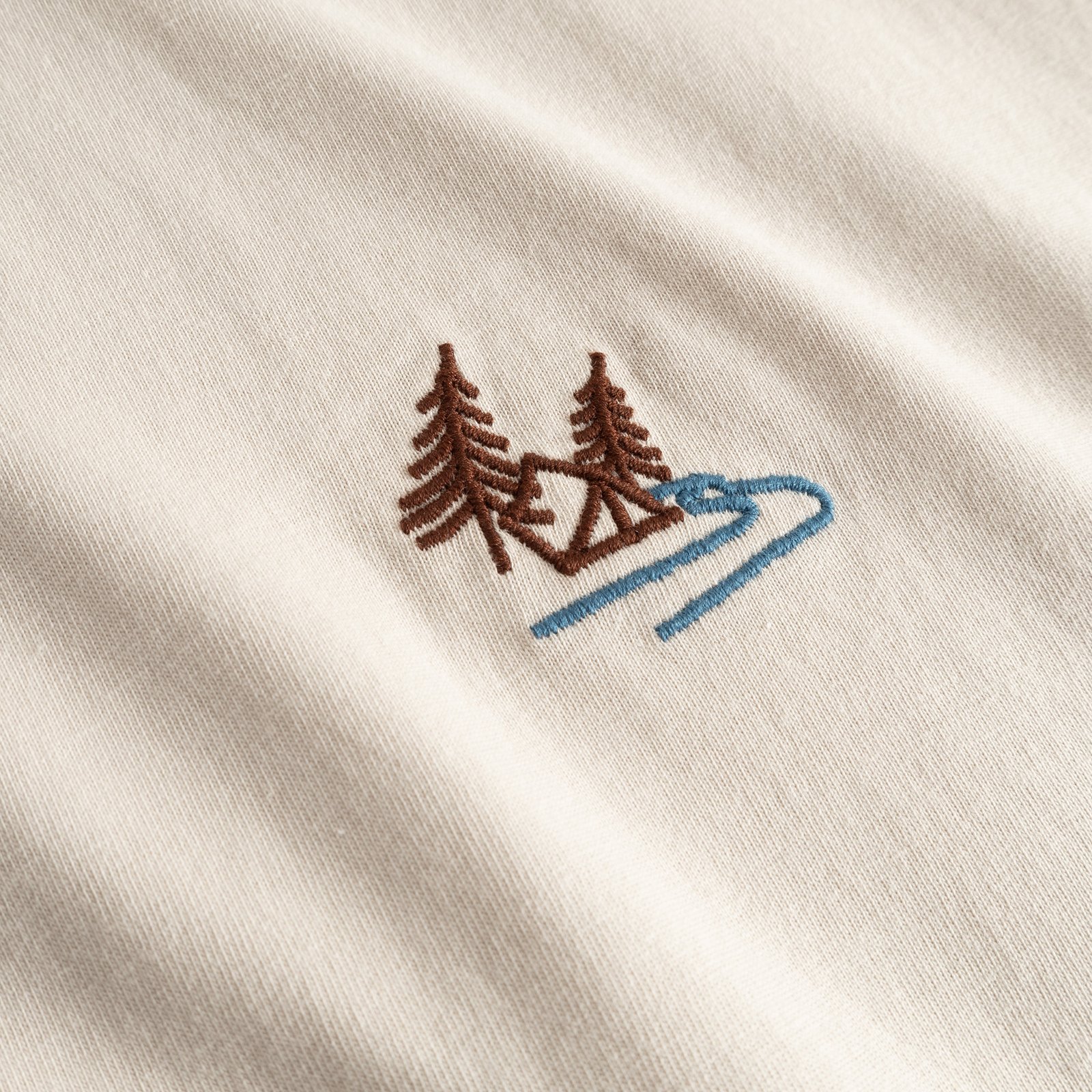 Close-up of the T-shirt Stockholm in Oat White, featuring the detailed Camp Creek embroidery of trees and a stream.