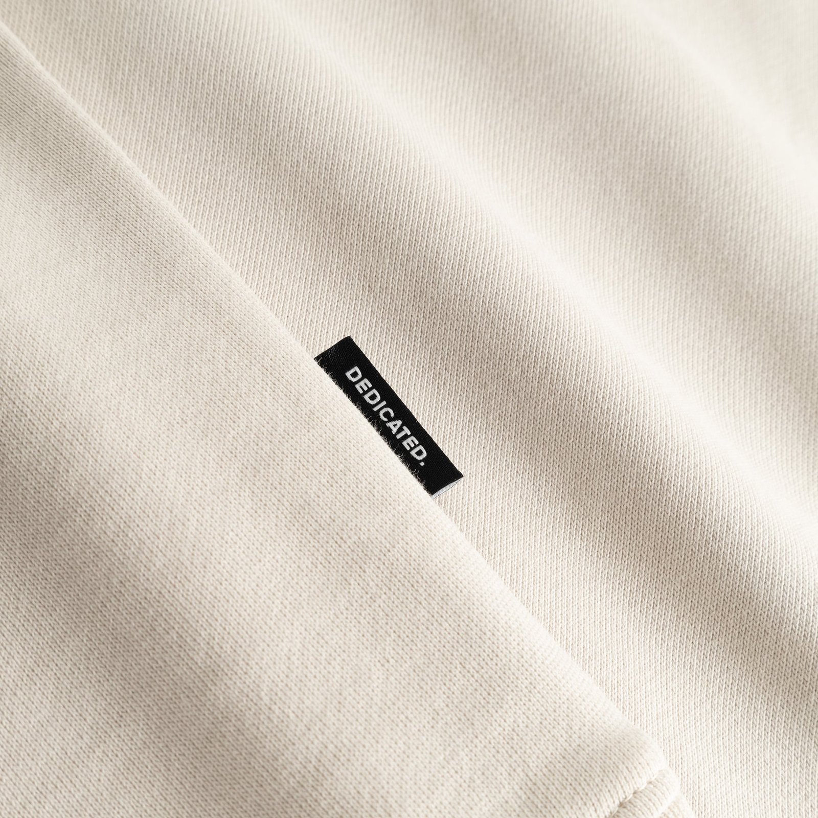 Close-up shot of the oat white Sweatshirt Malmoe, highlighting the soft fabric and the black Dedicated brand tag on the seam.