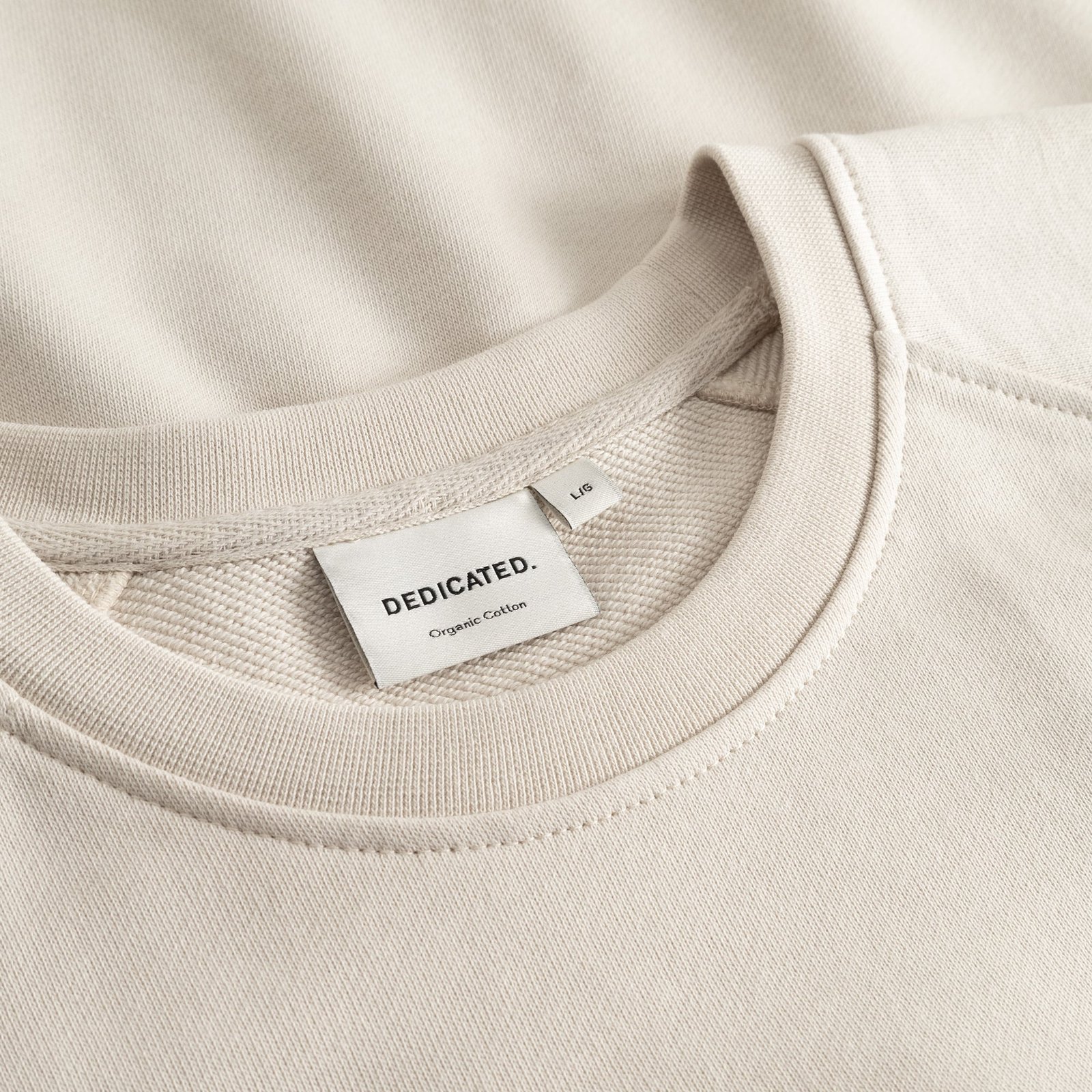 Detailed shot of the oat white Malmoe sweatshirt neckline, highlighting the soft organic cotton and Dedicated brand tag.