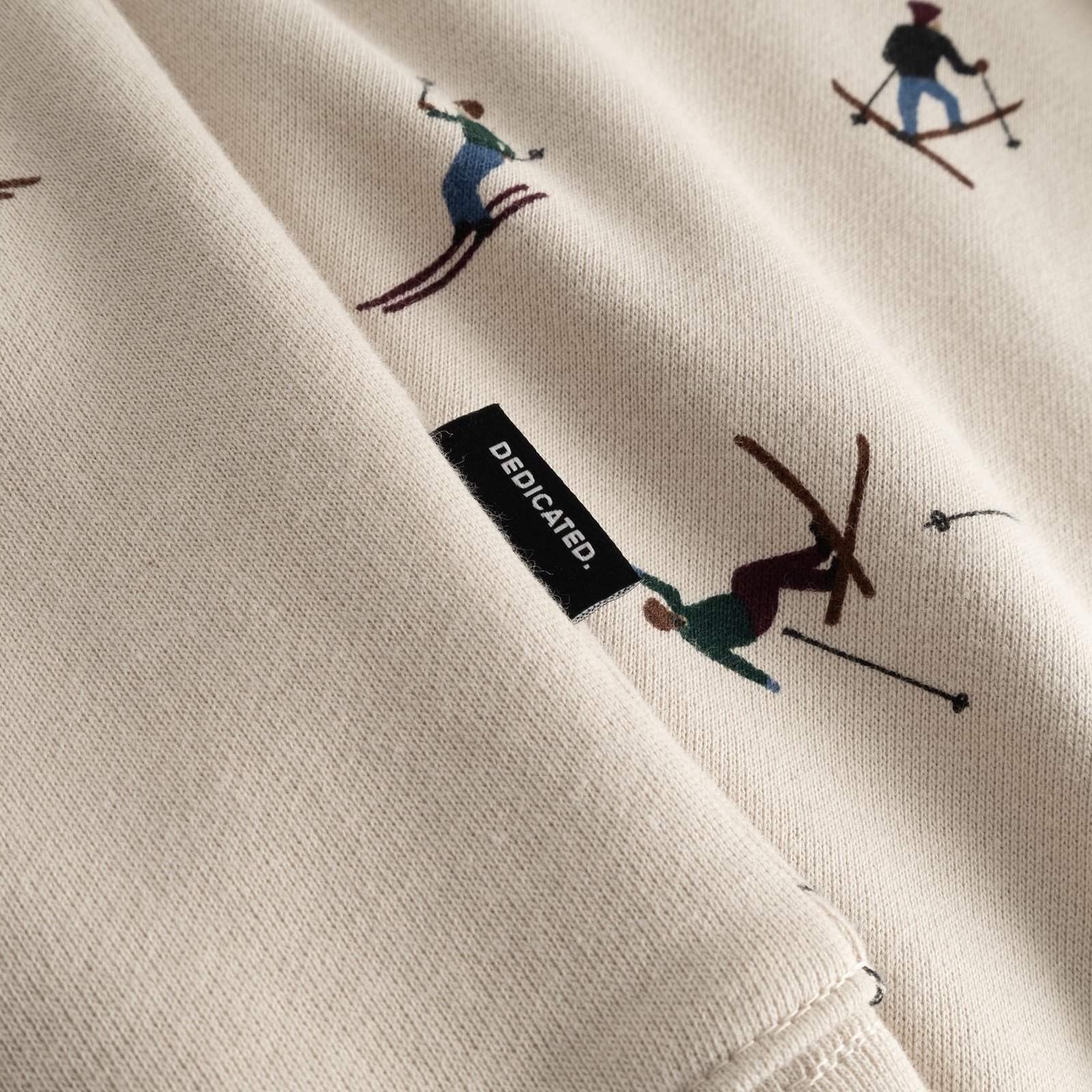 Close-up of the oat white Hoodie Falun Ski Team, featuring the all-over skier print and the black Dedicated brand tag.